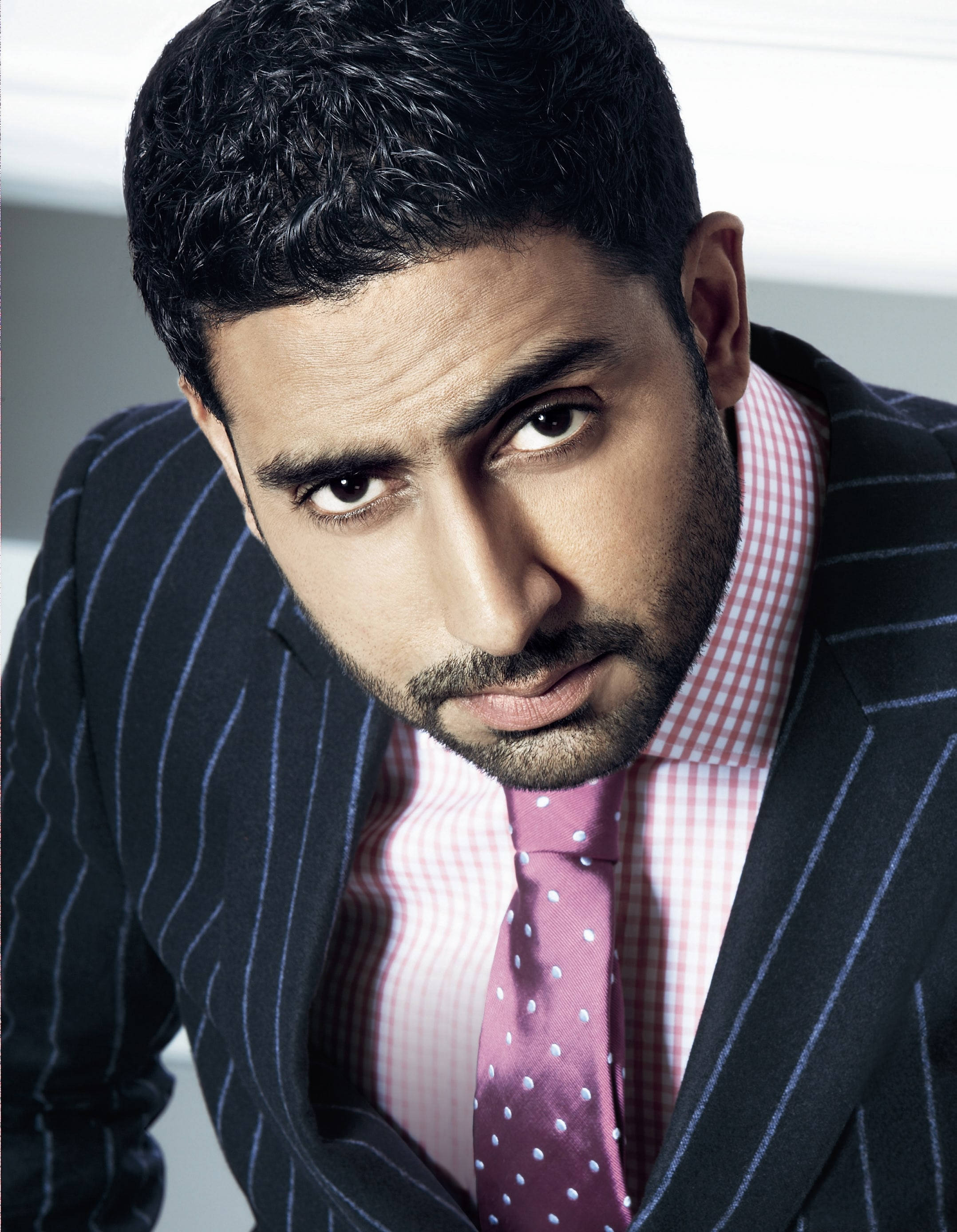 abhishek bachchan 桌布 壁紙 — 一位穿著筆挺、身穿細條紋西裝和圓點領帶的男子，帶著嚴肅的表情，強烈地凝視著鏡頭。