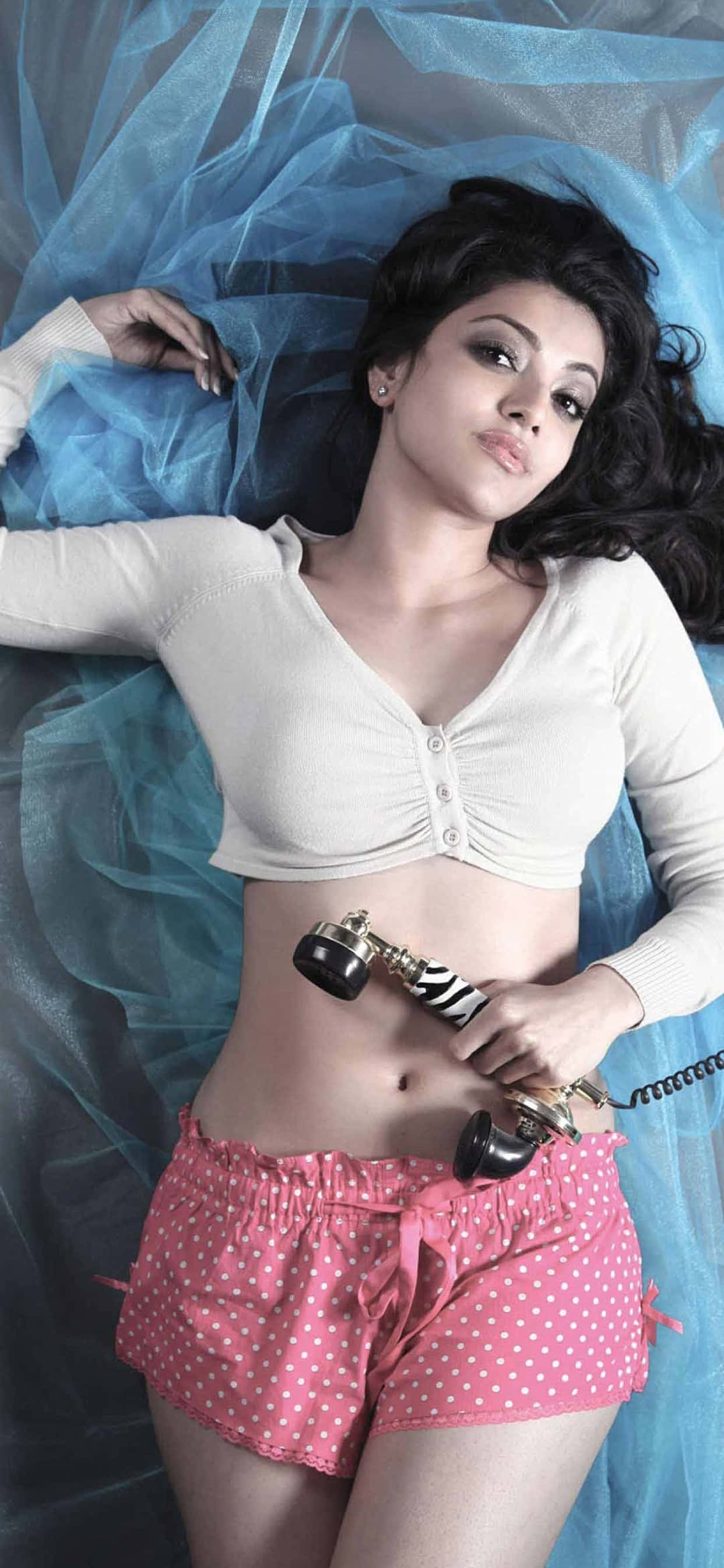 sexy babe 桌布 壁紙 — 一位穿著粉紅色圓點短褲和白色露臍上衣的女性躺在藍色薄紗上，手持復古電話聽筒。