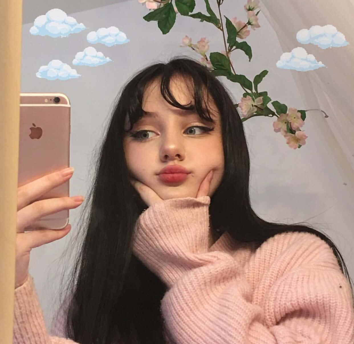 美少女動態圖 桌布 壁紙 — 一位穿著粉紅色毛衣的年輕女子在卡通雲朵和粉紅色花朵裝飾的背景前對著鏡子自拍。