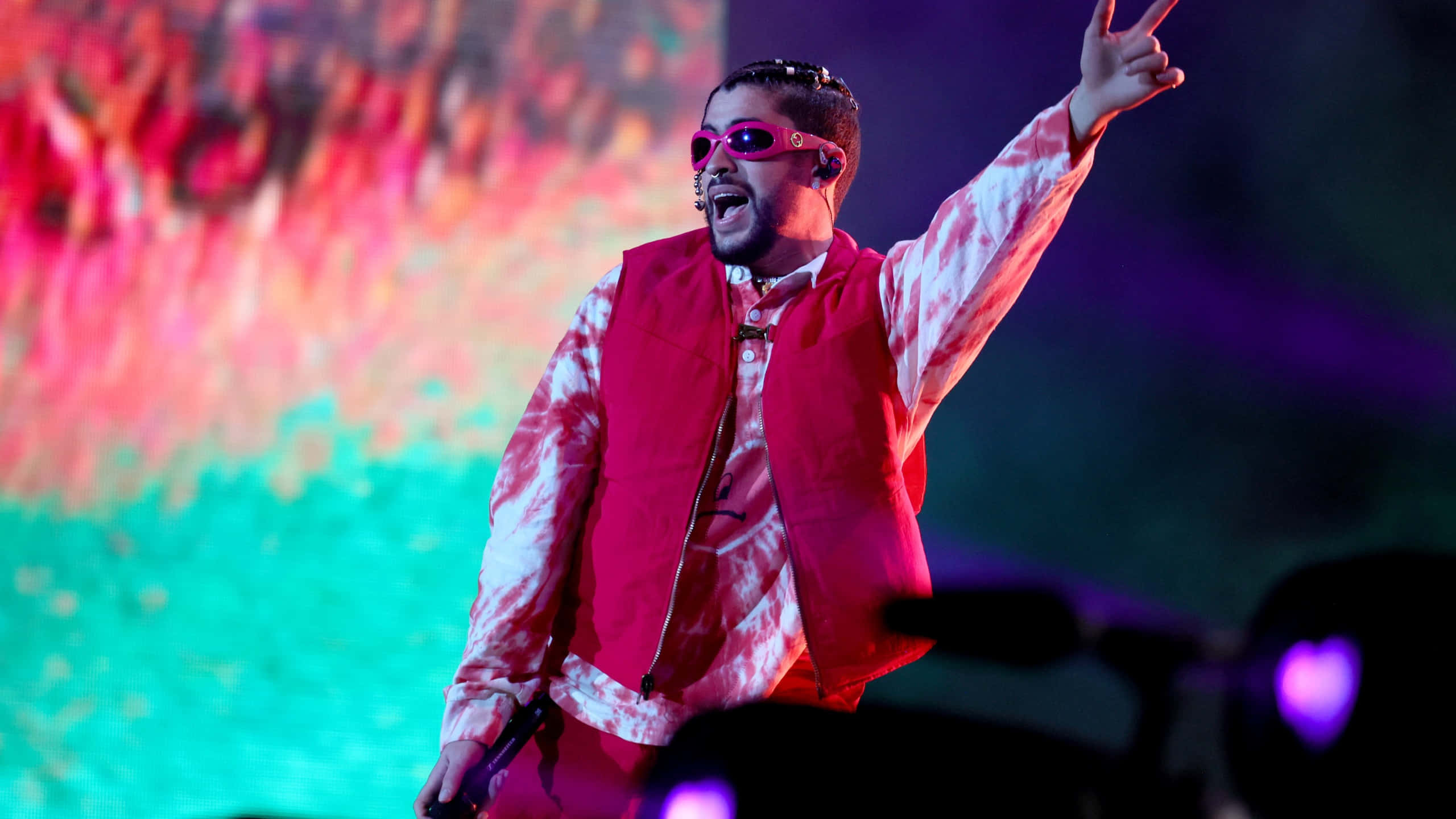 Coachella 桌布 壁紙 — 一位穿著粉紅色紮染服裝和太陽眼鏡的表演者在充滿活力的舞台燈光下為人群注入活力。