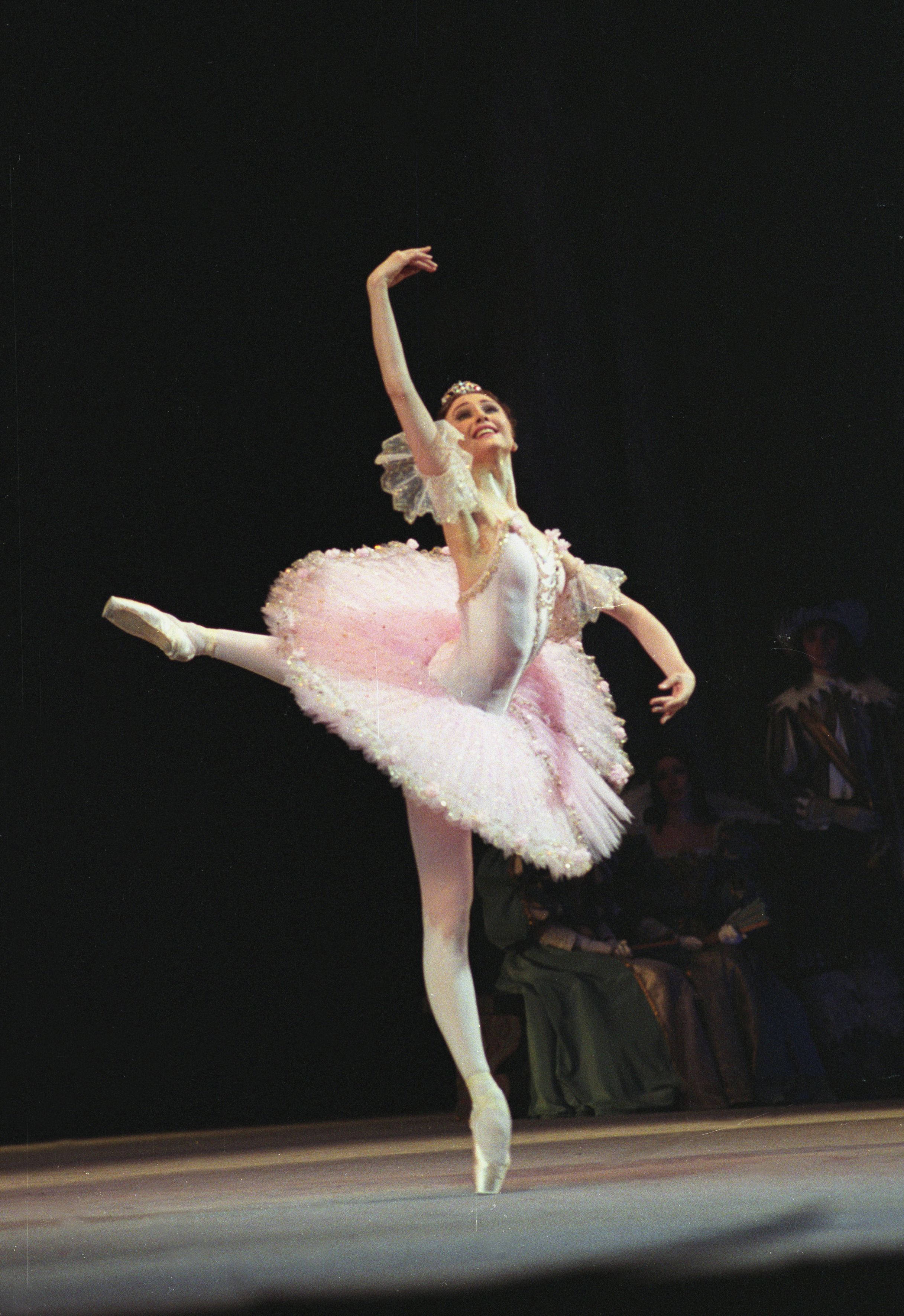 Ballet 桌布 壁紙 — 一位穿著粉紅色芭蕾舞裙的芭蕾舞者在戲劇性聚光燈下優雅地踮起腳尖平衡在舞台上。
