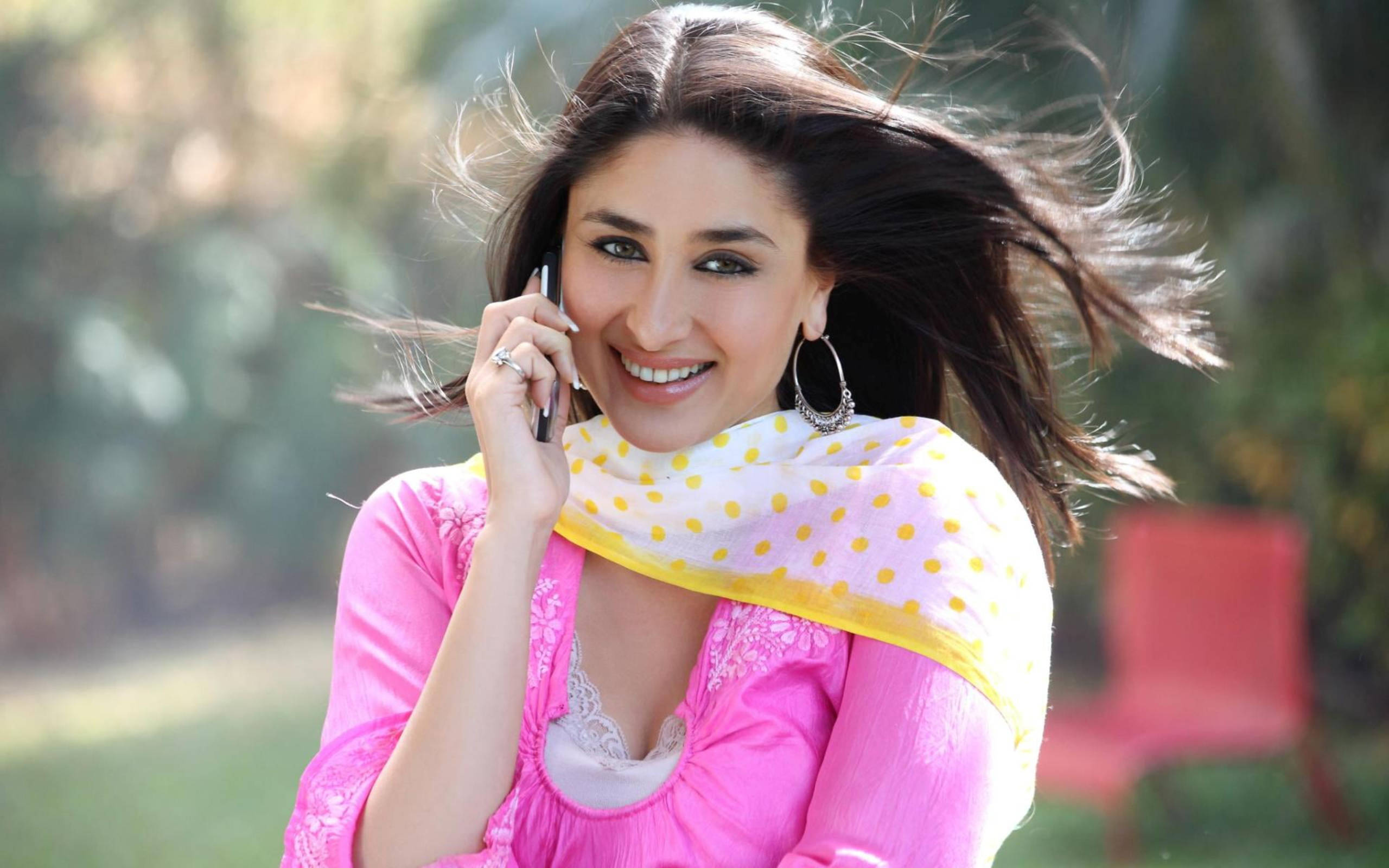 Kareena 桌布 壁紙 — 一位穿著粉紅色衣服、面帶微笑的女性在戶外打電話，風吹動她的頭髮。