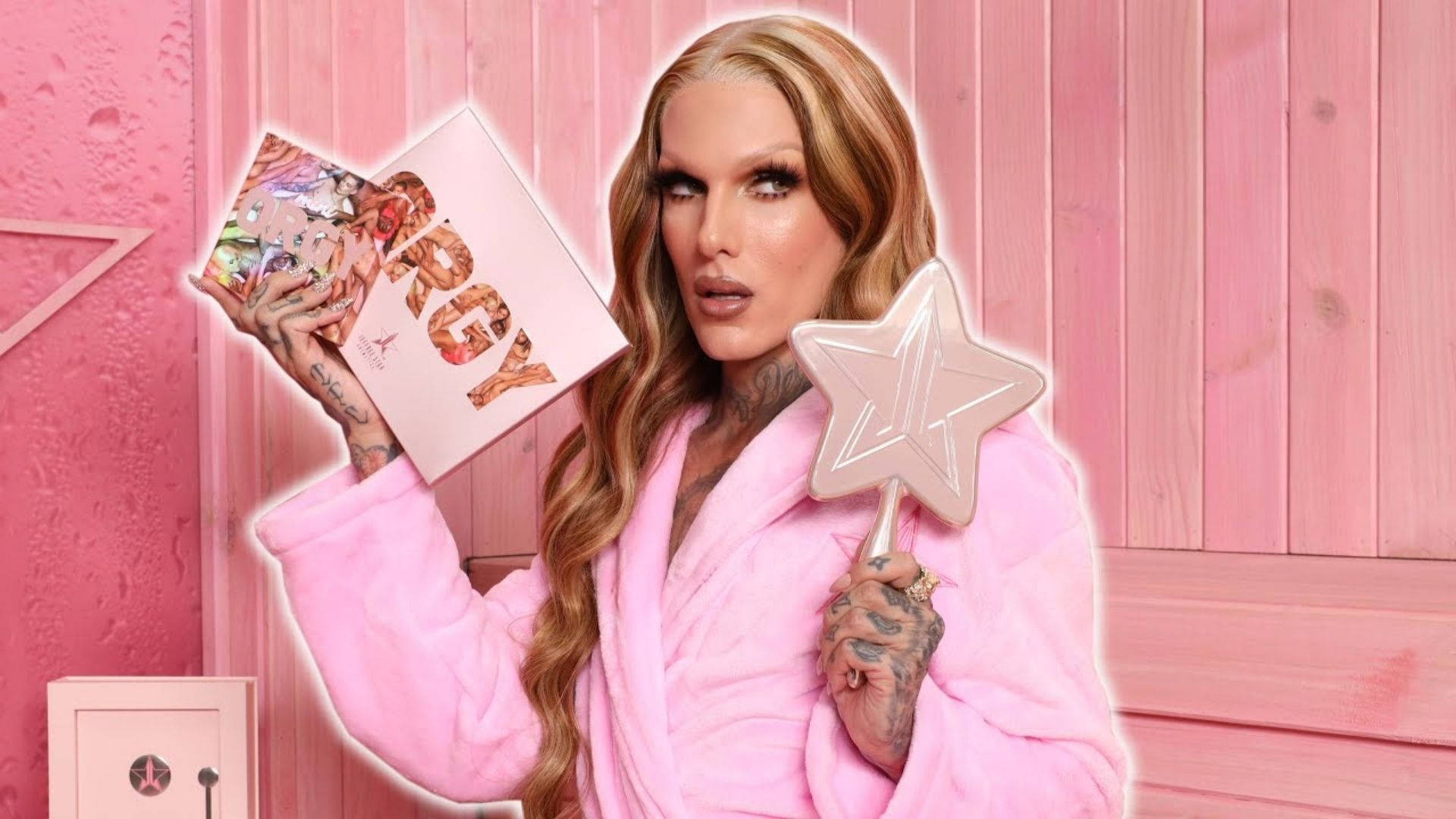 Jeffree Star 桌布 壁紙 — 一位穿著粉紅色長袍的變裝皇后，在粉紅色木牆前手持星星魔杖和化妝盤。