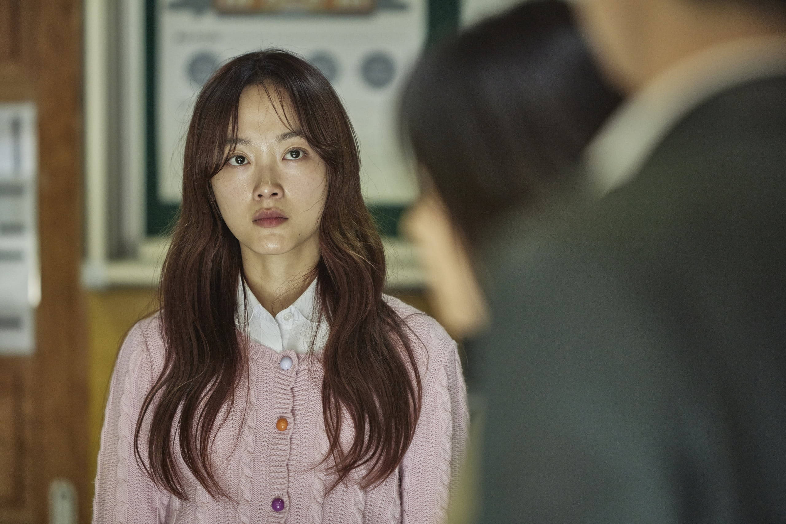 恐怖 桌布 壁紙 — 一位穿著粉紅色開襟毛衣的年輕女性在昏暗的室內環境中專注地凝視著另一個人。
