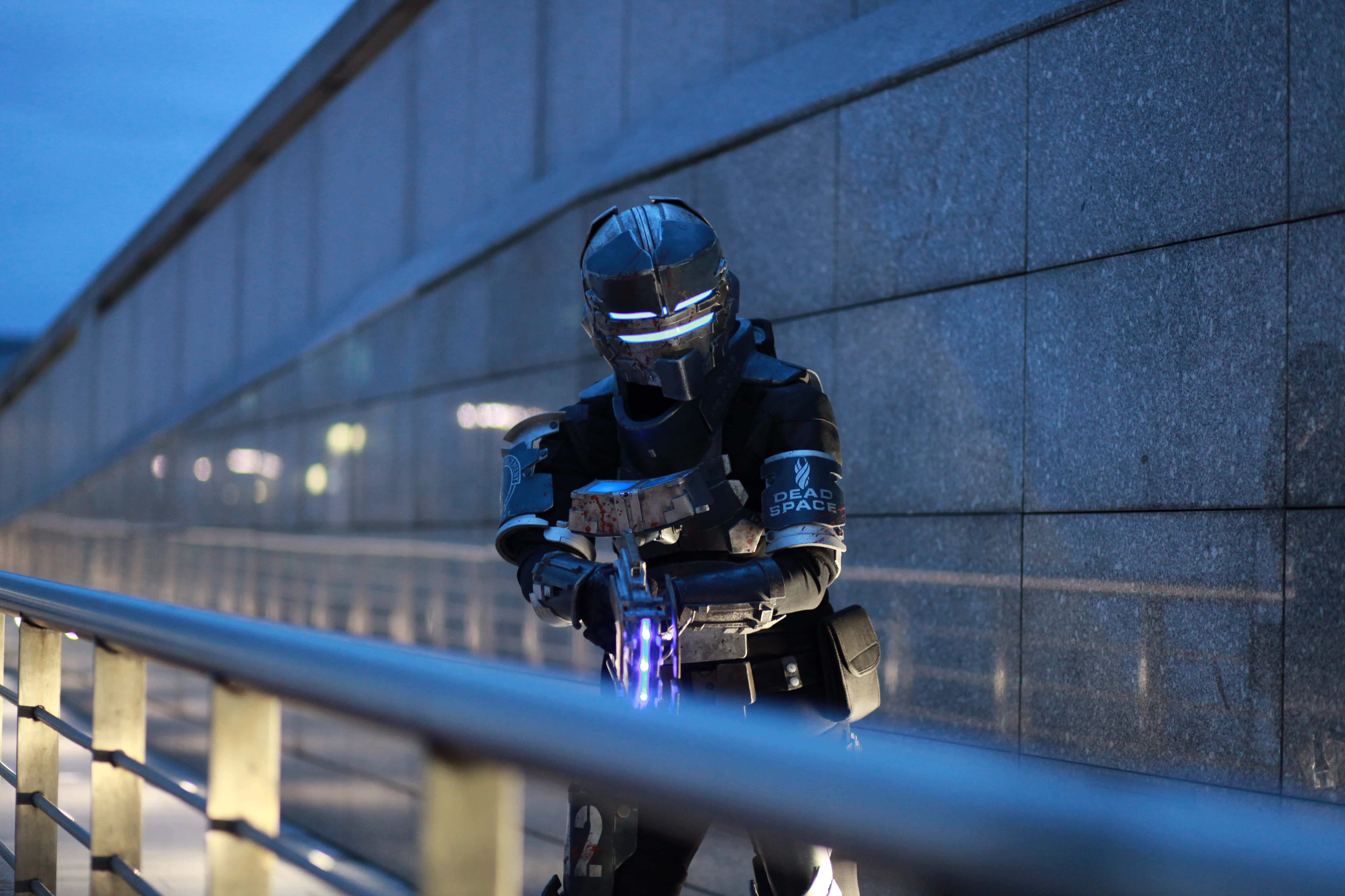 Dead Space 4K 桌布 壁紙 — 一位穿著精細 Dead Space 動力裝甲的 cosplayer 在黃昏時分警覺地站在現代混凝土牆旁。