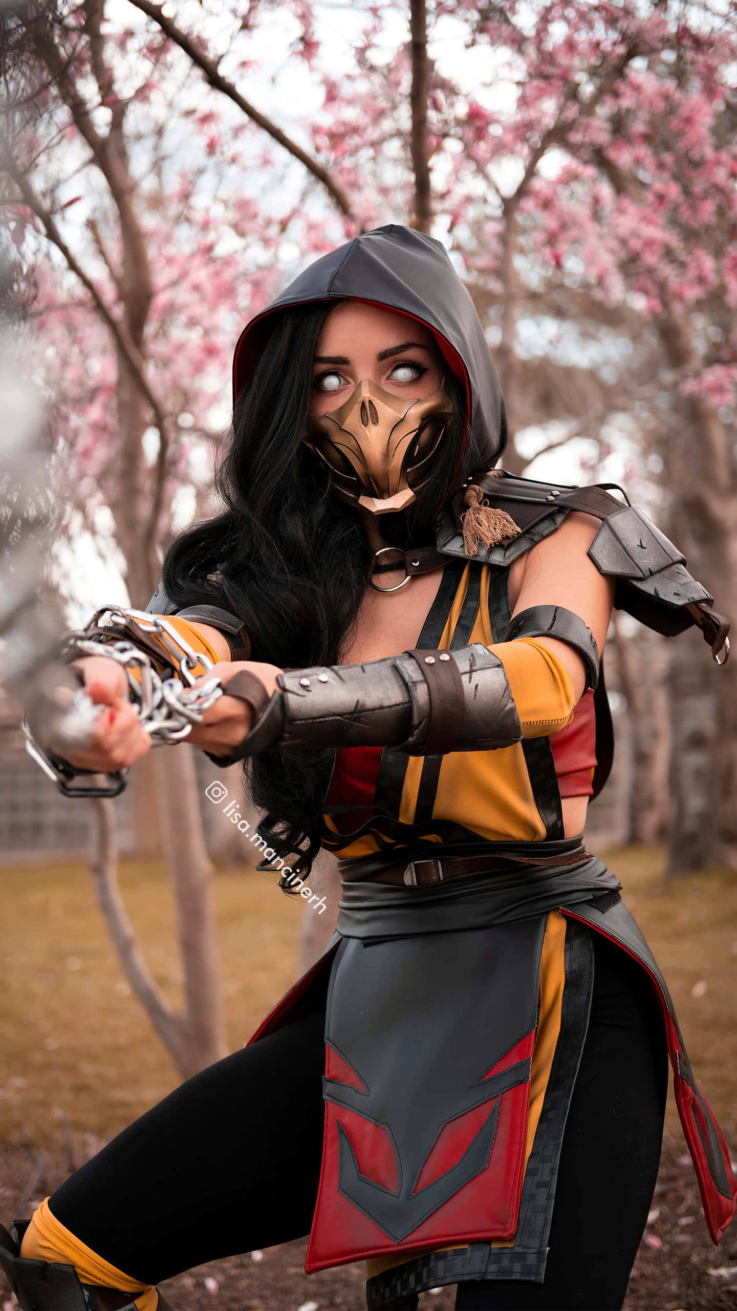 Mortal Kombat Cosplays 桌布 壁紙 — 一位穿著精細蠍子服裝的角色扮演者在盛開的粉紅色櫻花樹下擺出動感姿勢。