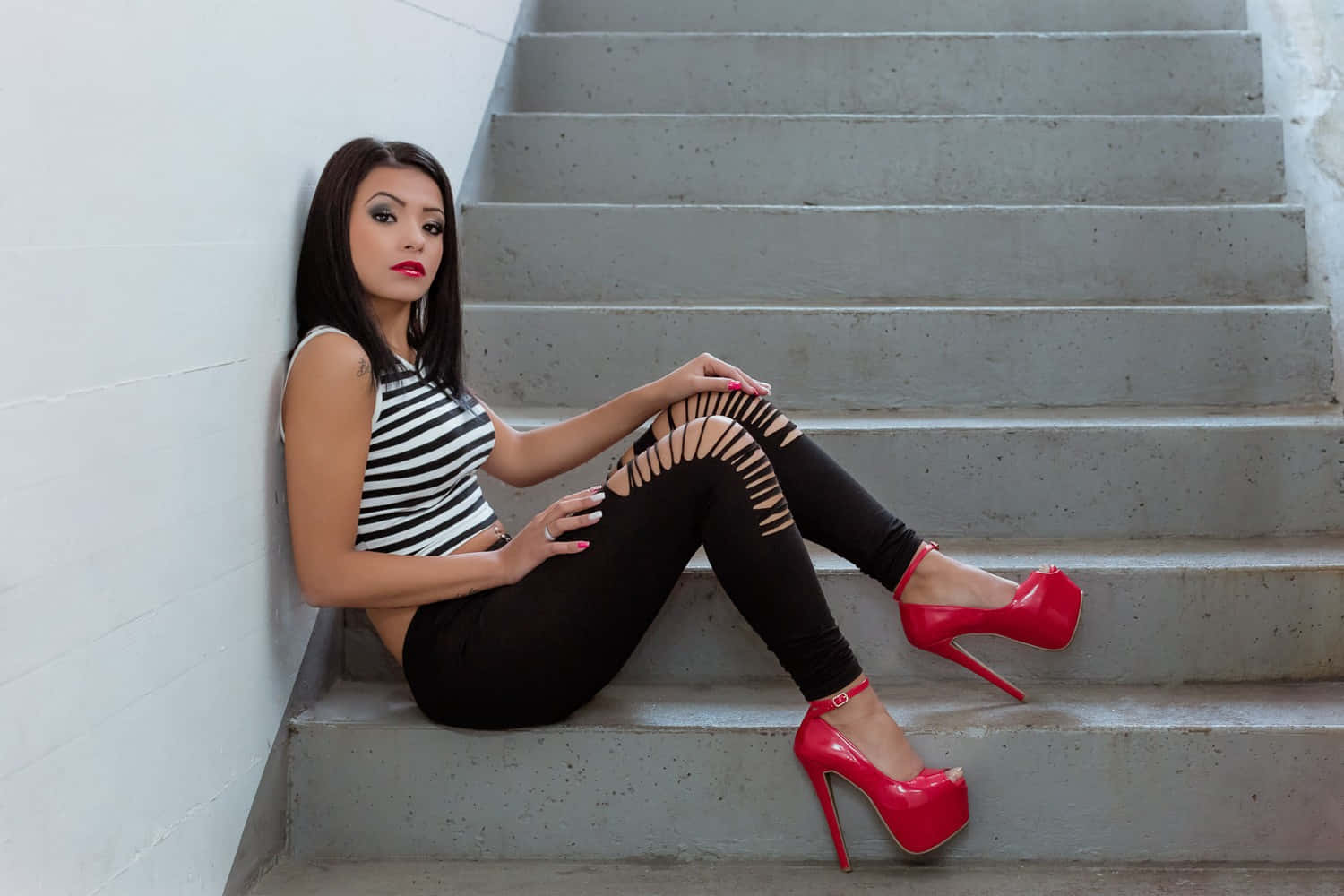 Red High Heels 桌布 壁紙 — 一位穿著紅色厚底高跟鞋和條紋上衣的女性自信地坐在白色牆壁前的混凝土樓梯上。