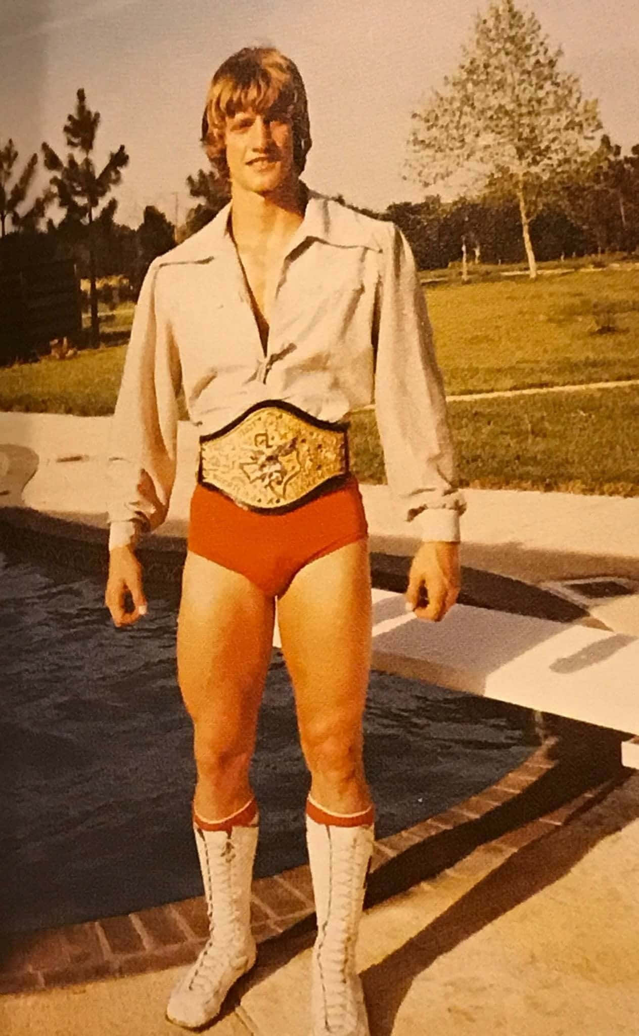 Champion 桌布 壁紙 — 一位穿著紅色短褲和白色靴子的復古摔角手，戴著金色冠軍腰帶站在泳池旁。
