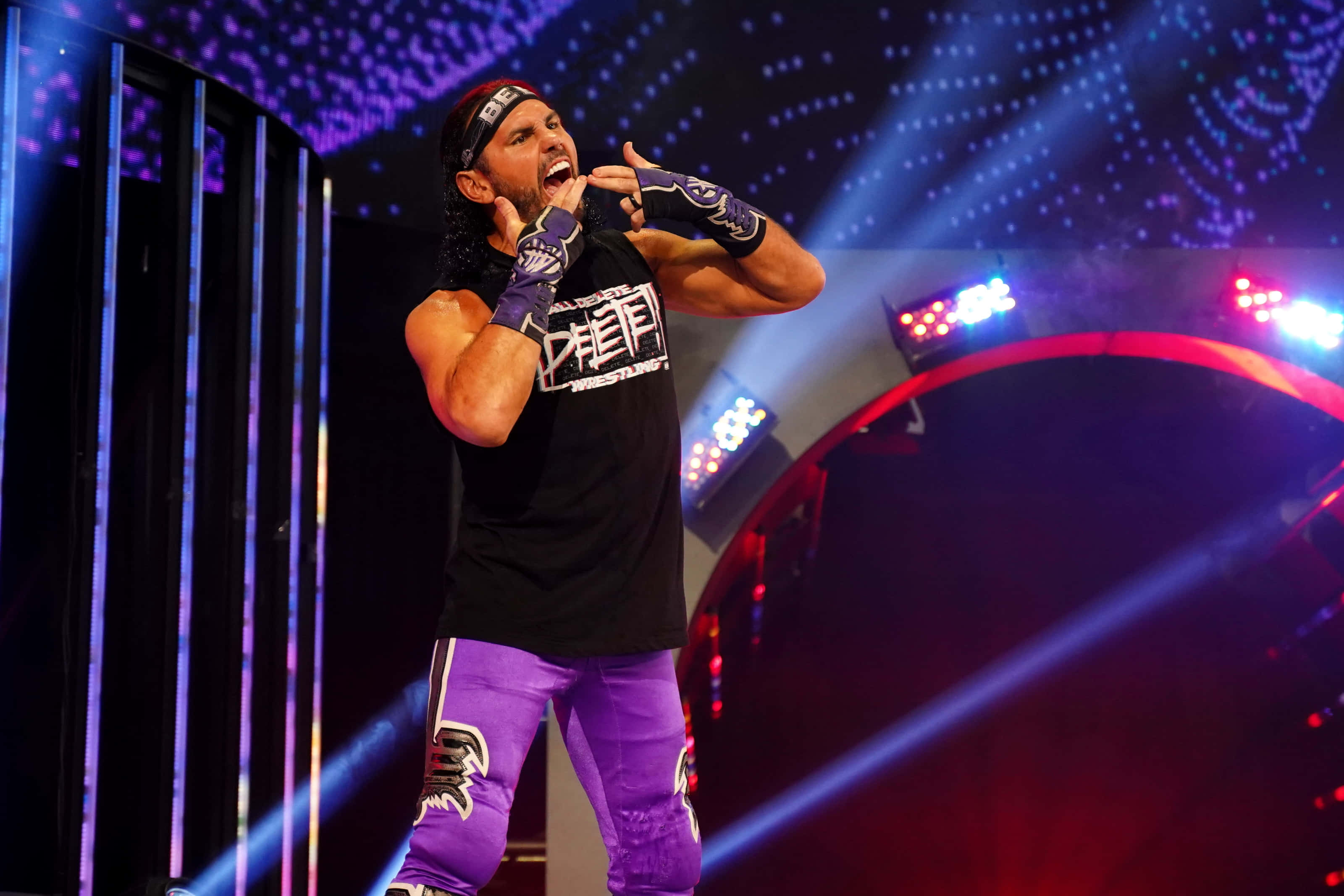 WWE 桌布 壁紙 — 一位穿著紫色褲子和黑色襯衫的摔角手在充滿活力的舞台燈光、雷射光束和星空背景下熱情地尖叫。