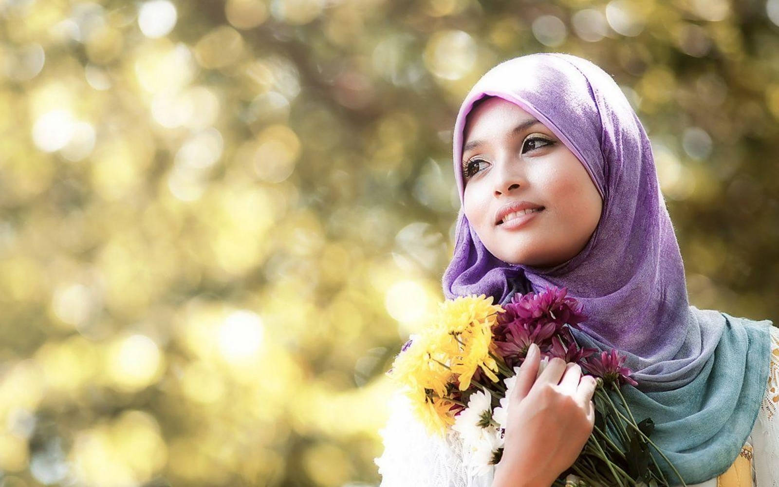 muslim 桌布 壁紙 — 一位穿著紫色頭巾的年輕女性，手持一束黃色和紫色的花，在陽光照射的金色散景背景下溫柔微笑。