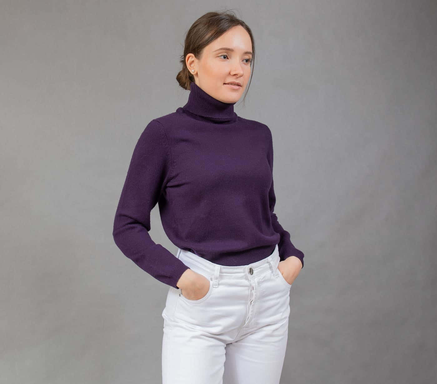 Purple Turtle-neck Sweater 桌布 壁紙 — 一位穿著紫色高領毛衣和白色牛仔褲的女性，雙手插袋，自信地站在中性灰色攝影棚背景前。