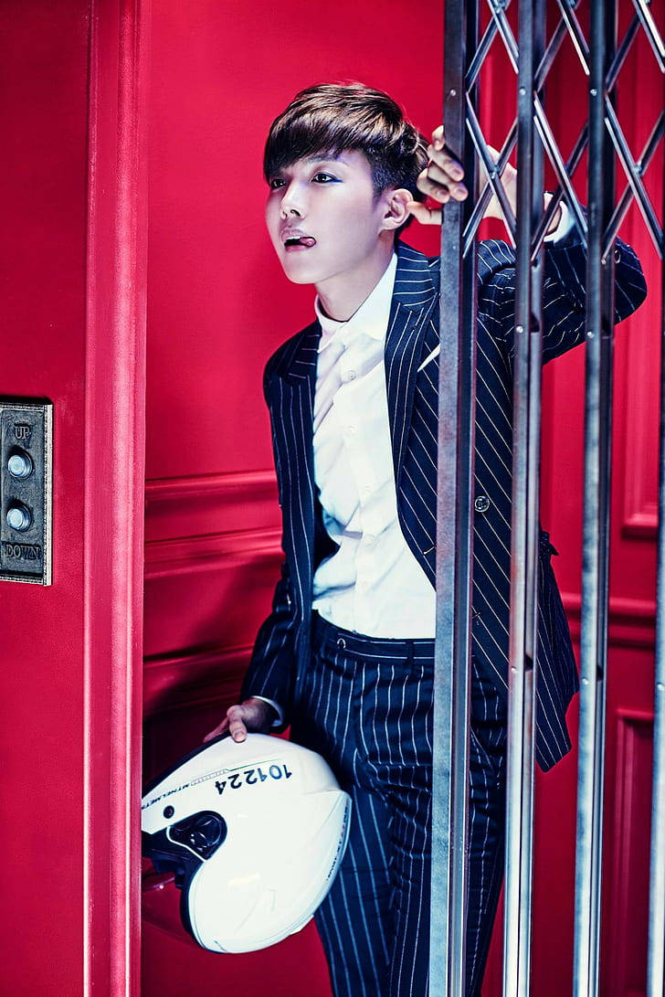 j-hope 桌布 壁紙 — 一位穿著細條紋西裝的年輕男子，在充滿活力的紅色電梯內，靠著金屬欄杆，手持白色頭盔。