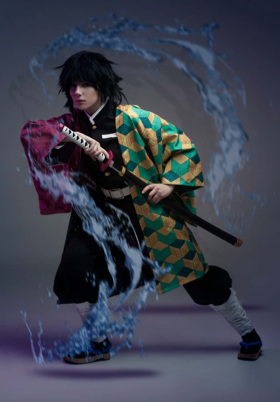 Demon Slayer Corps 桌布 壁紙 — 一位穿著綠色、金色和紅色和服的Cosplayer揮舞著劍，藍色的水在灰色背景上戲劇性地飛濺。