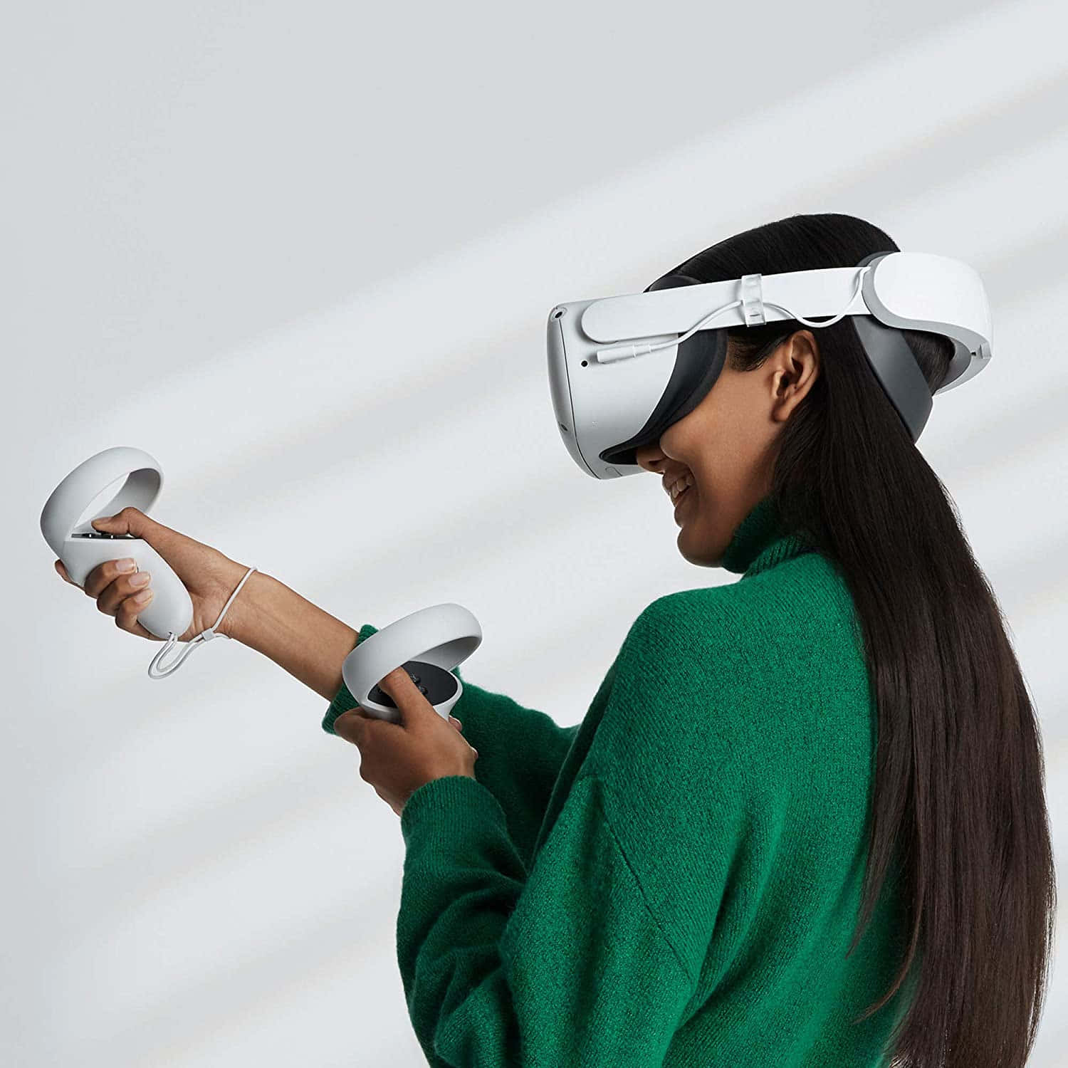 Oculus Quest 2 桌布 壁紙 — 一位穿著綠色毛衣的女性，戴著白色VR頭戴式裝置，手持控制器，在簡約的白色背景前微笑。