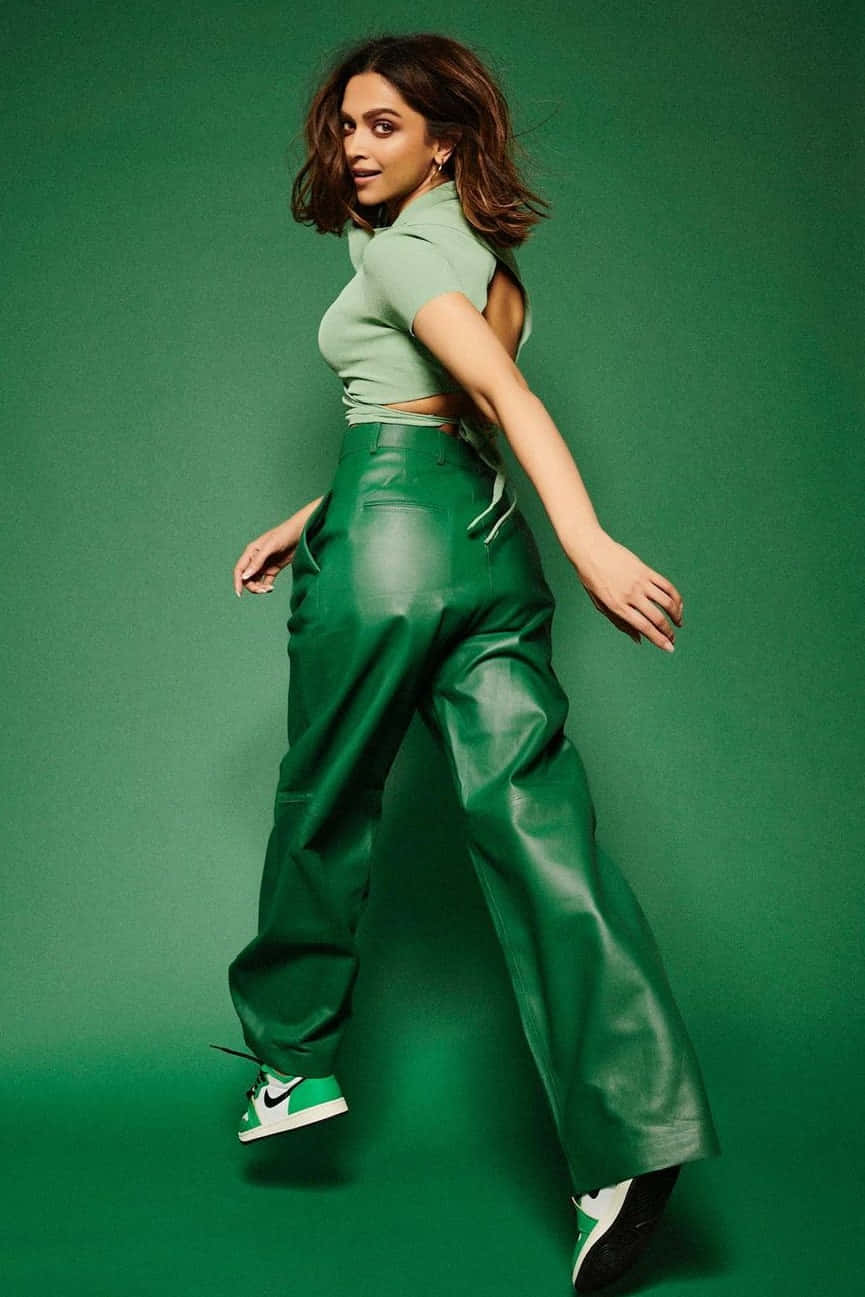 Green Fashion 桌布 壁紙 — 一位穿著綠色皮褲和露臍上衣的女性在純綠色工作室背景前自信地擺姿勢。