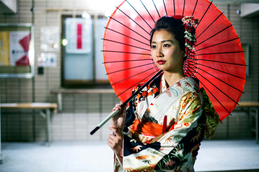 Japanese Women 桌布 壁紙 — 一位穿著花卉和服的女士站在瓷磚室內空間，手持鮮紅色陽傘。