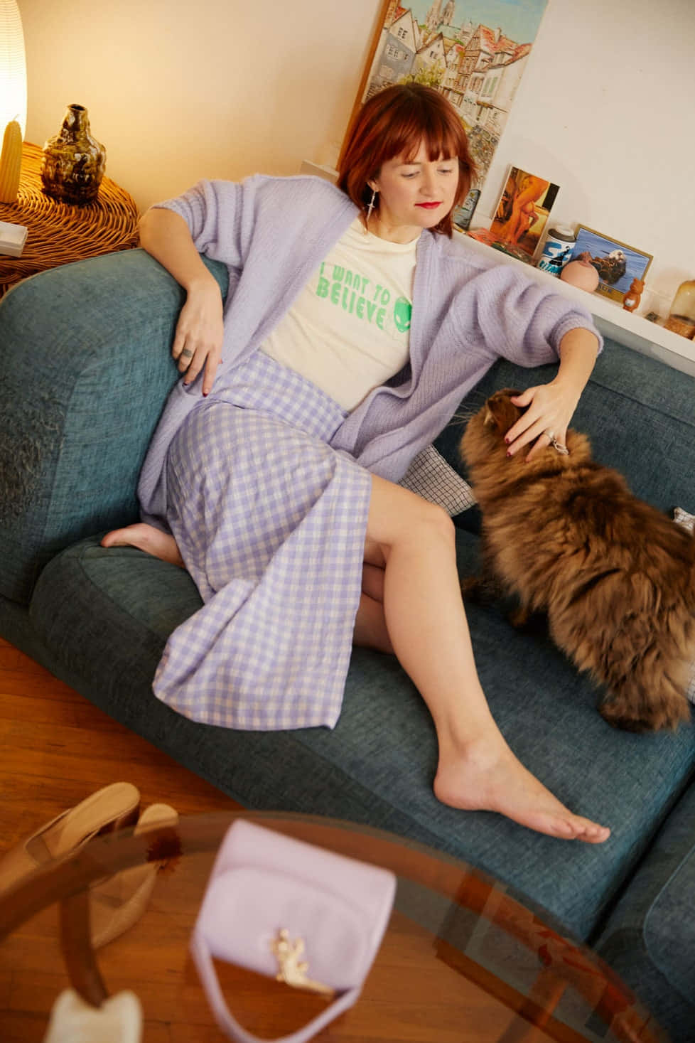 Woman 桌布 壁紙 — 一位穿著薰衣草色開襟衫和格子裙的女性在溫暖舒適的客廳裡，躺在藍色沙發上撫摸一隻蓬鬆的棕色貓咪。