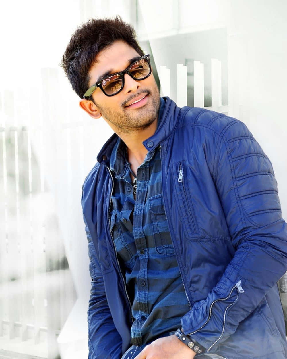 Allu Arjun 桌布 壁紙 — 一位穿著藍色外套和太陽眼鏡的時尚男士，在明亮的白色建築背景下自信地微笑。