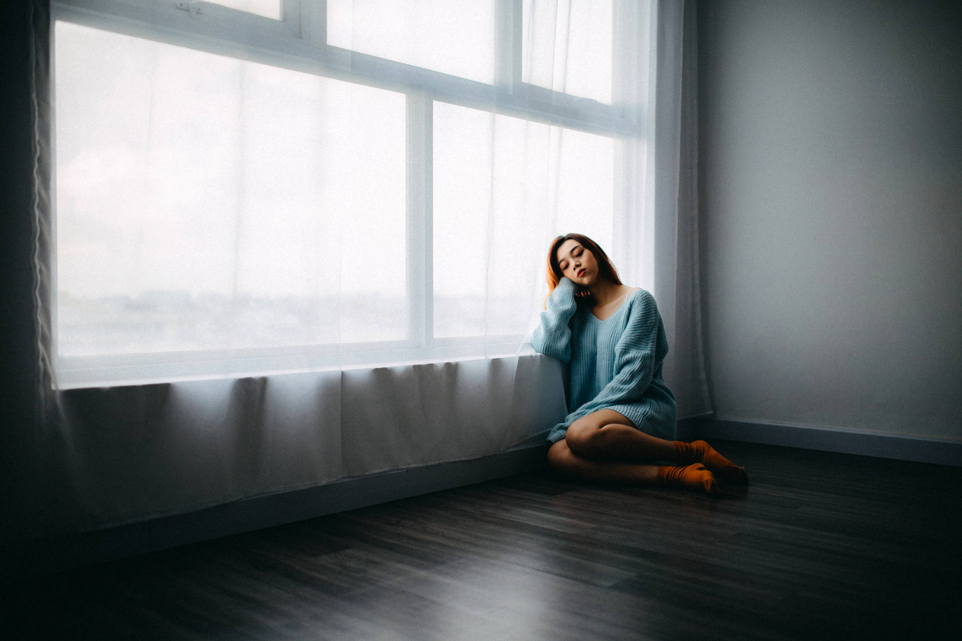 一位穿著藍色毛衣的女性靜靜地坐在大窗戶旁，窗簾輕薄。 — 黑暗悲傷動圖 壁紙