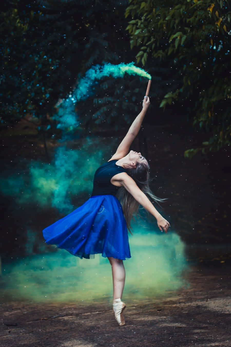 dancer 桌布 壁紙 — 一位穿著藍色裙子的芭蕾舞者在森林中優雅地跳躍，同時從一根棍子中釋放出發光的青綠色煙霧。