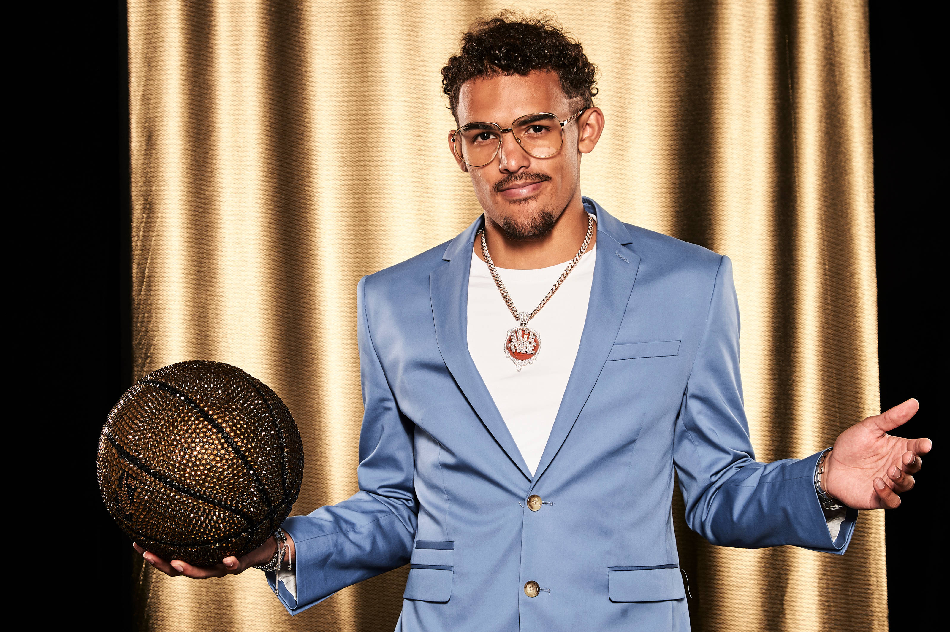 Trae Young 桌布 壁紙 — 一位穿著藍色西裝的時尚男士，在金色窗簾背景下拿著閃閃發光的籃球。