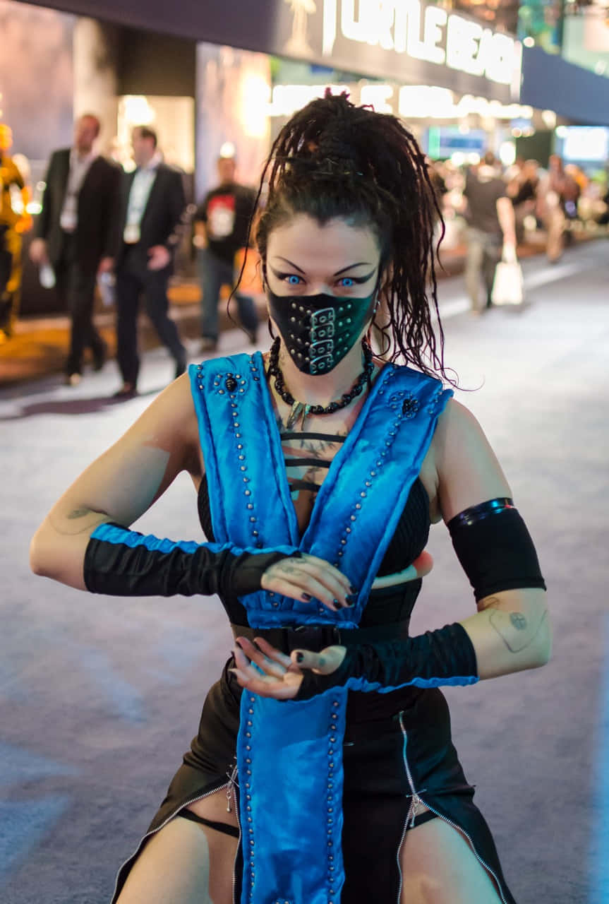 Mortal Kombat Cosplays 桌布 壁紙 — 一位穿著藍黑色Mortal Kombat服裝的角色扮演者在會議上自信地擺姿勢，戴著面具和辮子頭。