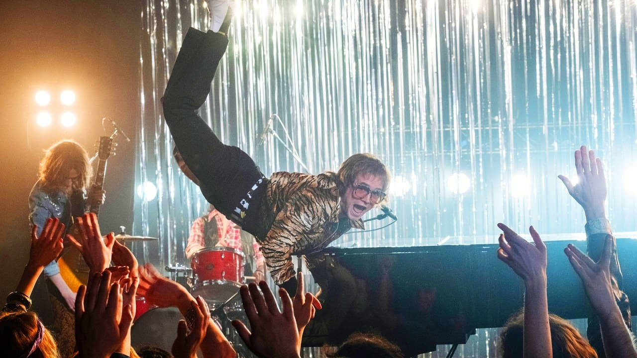 Rocketman 桌布 壁紙 — 一位穿著虎紋外套的表演者凌空躍過觀眾，舞台燈光穿過他們背後的銀色窗簾照射出來。