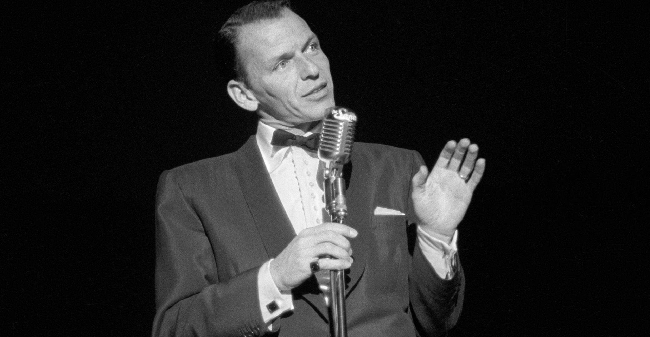 Sinatra 桌布 壁紙 — 一位穿著西裝、充滿魅力的男歌手在舞台上手持經典麥克風的復古黑白肖像。