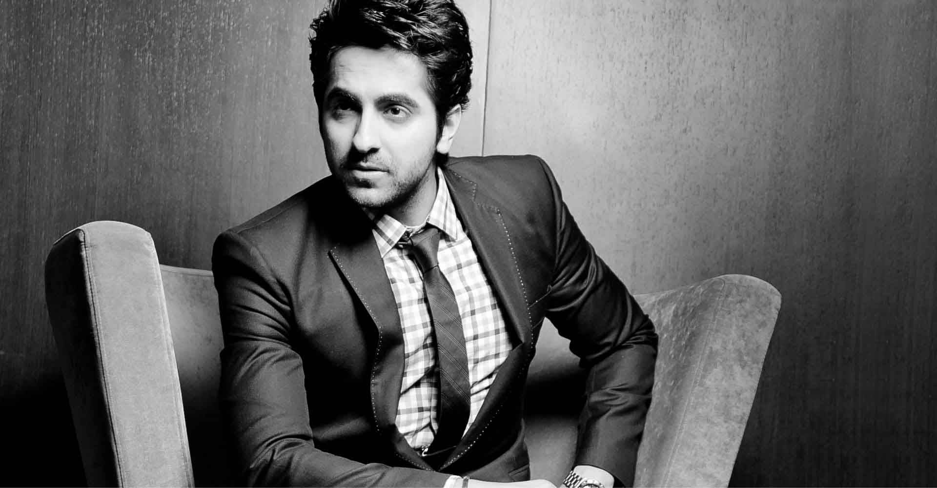 ayushmann khurrana 桌布 壁紙 — 一位穿著西裝、打扮俐落的男士自信地坐在椅子上，背景是帶有紋理的牆壁，呈現出充滿氛圍感的黑白肖像。