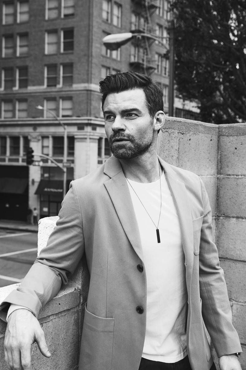 Daniel Gillies 桌布 壁紙 — 一位穿著西裝外套的時尚男士，在單色城市街景中靠著混凝土牆。