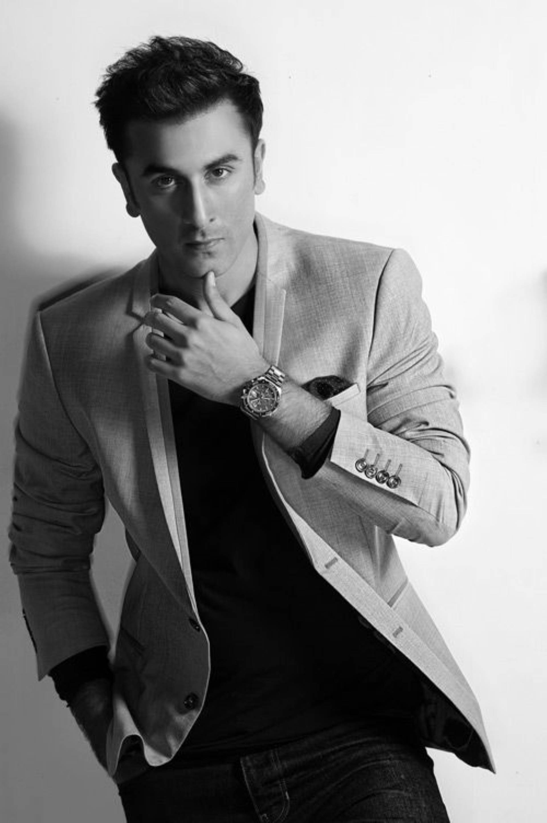 Ranbir Kapoor 桌布 壁紙 — 一位穿著西裝外套的時尚男士在純色背景前自信地擺姿勢，一隻手靠近下巴。