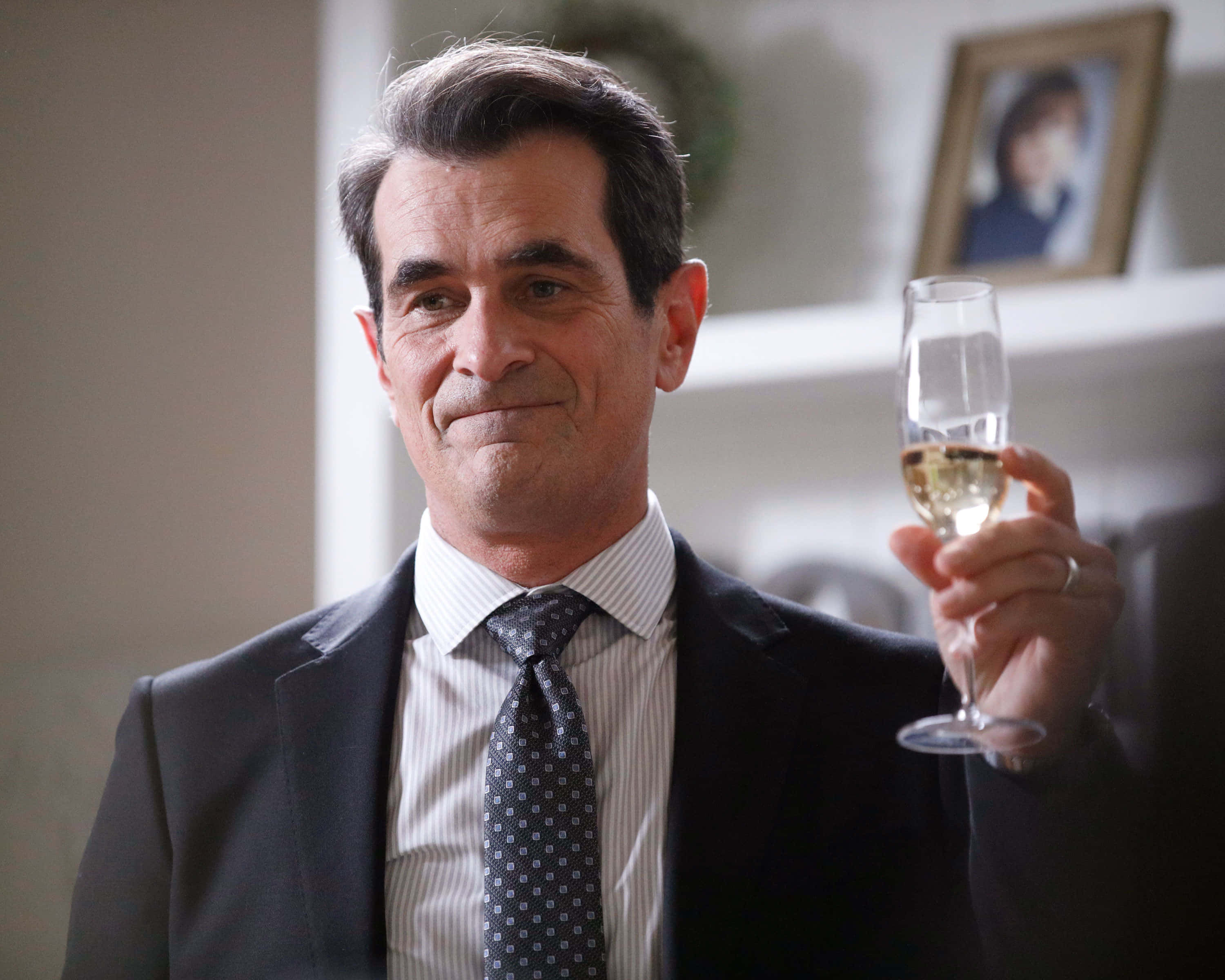 Ty Burrell 桌布 壁紙 — 一位穿著西裝的中年男子在室內微笑著手持一杯香檳。