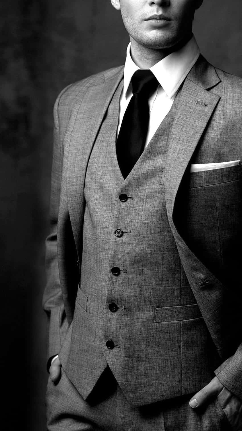 style 桌布 壁紙 — 一位穿著質感三件套西裝、衣著講究的男子，雙手插袋，自信地站在深色攝影棚背景前。