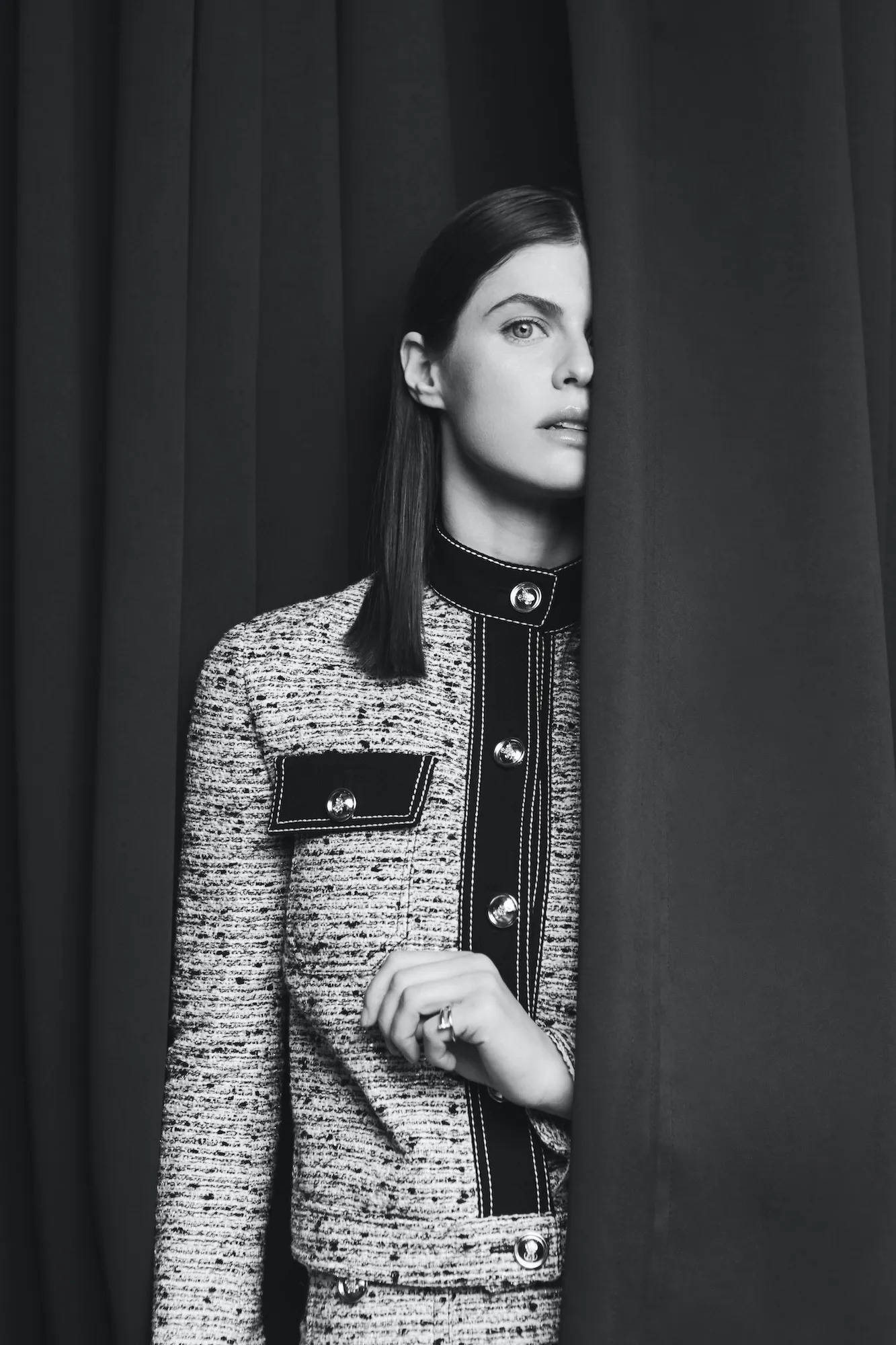 Alexandra 桌布 壁紙 — 一位穿著質感粗花呢外套的女性從深色窗簾後探出頭來，呈現鮮明的黑白肖像。