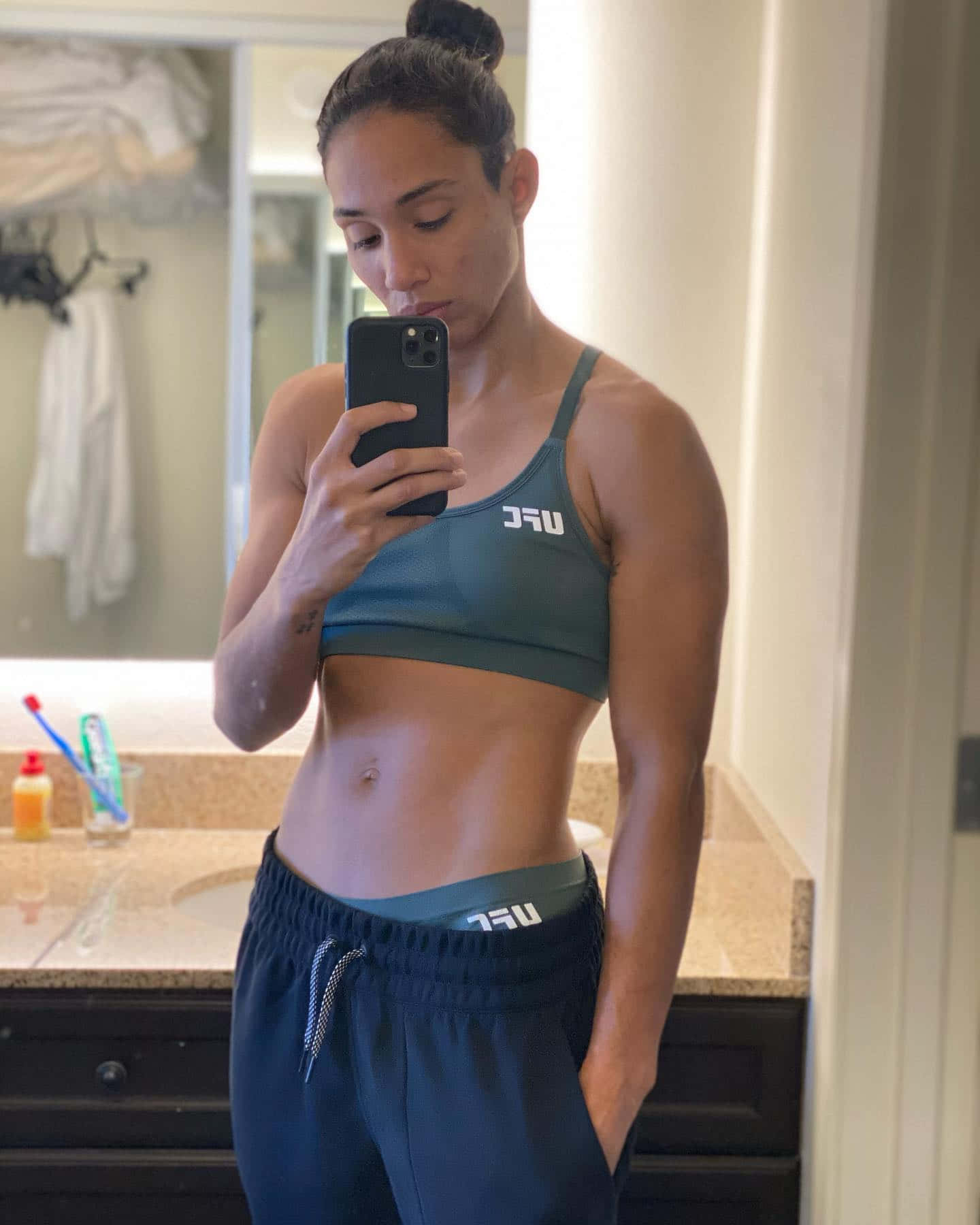 MMA 桌布 壁紙 — 一位穿著運動服的健美女性在光線柔和且可見洗漱用品的浴室中對著鏡子自拍。
