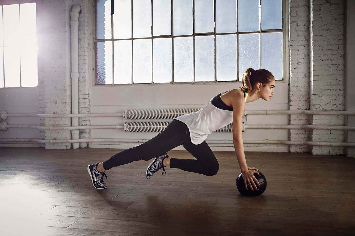 Exercise 桌布 壁紙 — 一位穿著運動服的女性在明亮工業風格的健身房中，使用藥球進行動態鍛煉，健身房有大窗戶。