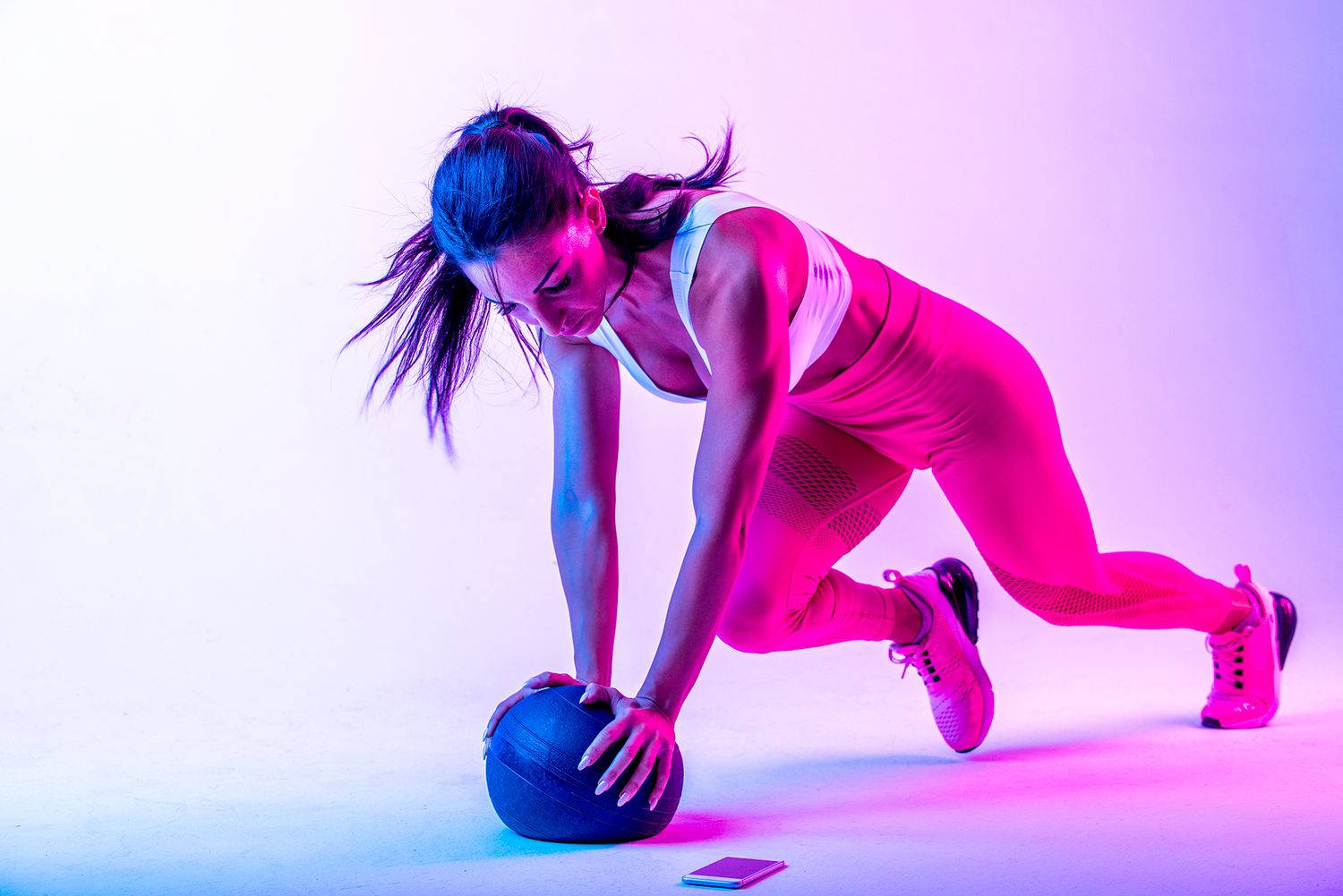 Exercise 桌布 壁紙 — 一位穿著運動服的女性在霓虹粉紅和藍色工作室燈光下，用藥球進行動態鍛煉。