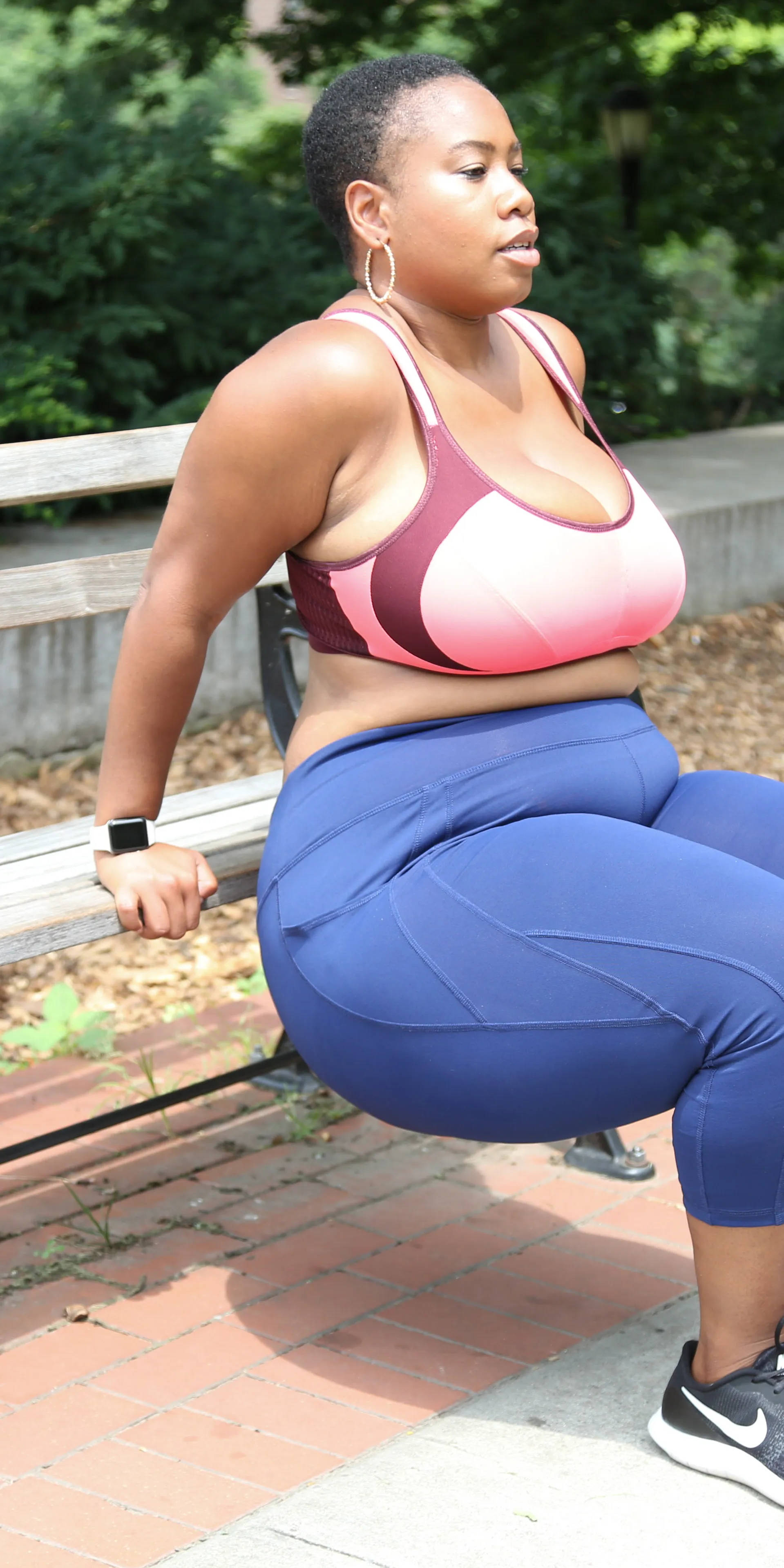 Exercise 桌布 壁紙 — 一位穿著運動服的女性坐在公園長椅上，周圍是綠化和磚鋪路面，在明亮的日光下。
