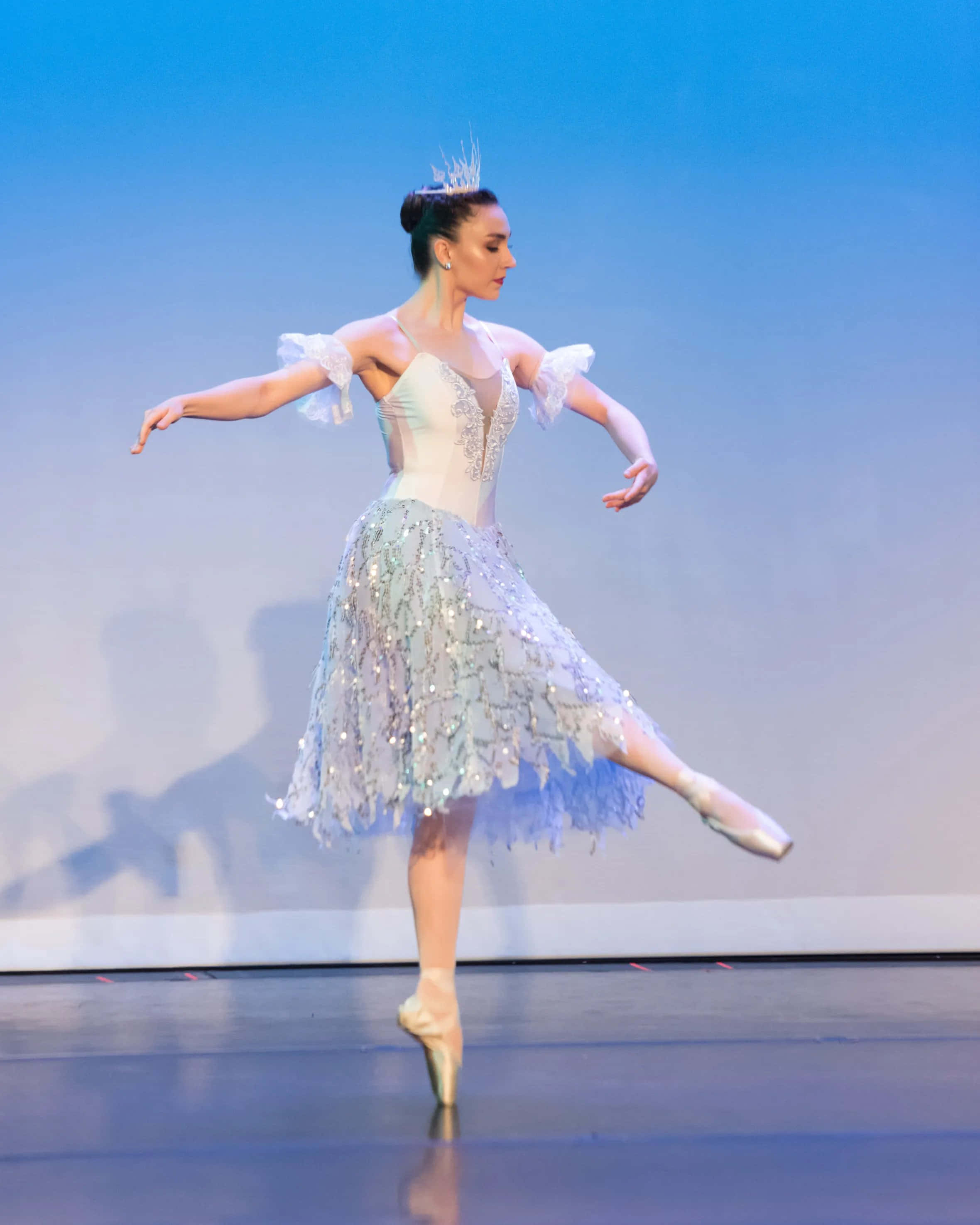 dancer 桌布 壁紙 — 一位穿著閃亮銀色芭蕾舞裙的芭蕾舞者，在柔和的藍色燈光下，優雅地踮起腳尖在舞台上保持平衡。