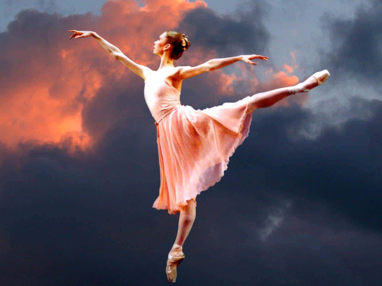 Ballet 桌布 壁紙 — 一位穿著飄逸粉紅色芭蕾舞裙的芭蕾舞者，在戲劇性的夕陽天空和火紅橙色雲彩的襯托下優雅地跳躍。