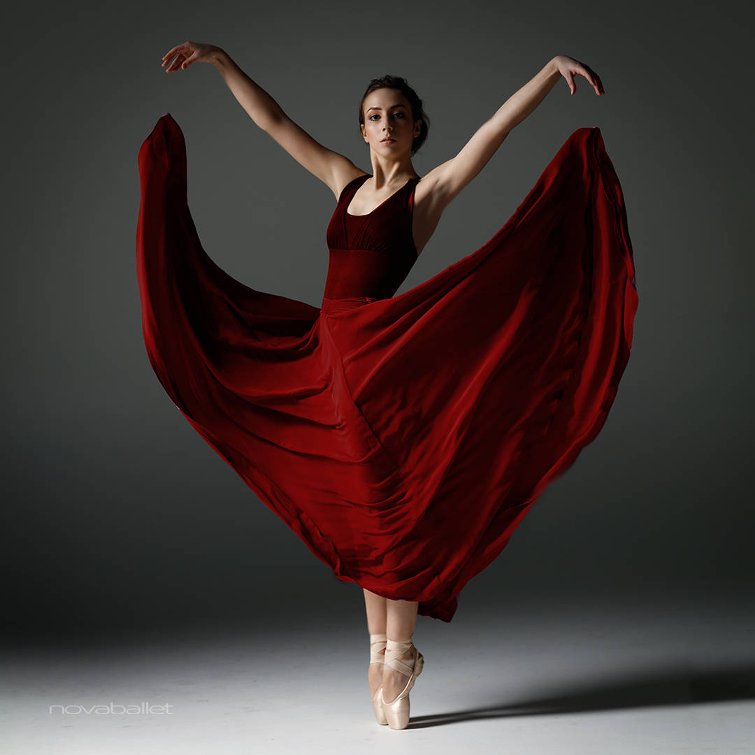 dancer 桌布 壁紙 — 一位穿著飄逸紅裙的芭蕾舞者踮起腳尖，雙臂高舉，布料在她周圍旋轉，背景是昏暗的攝影棚。