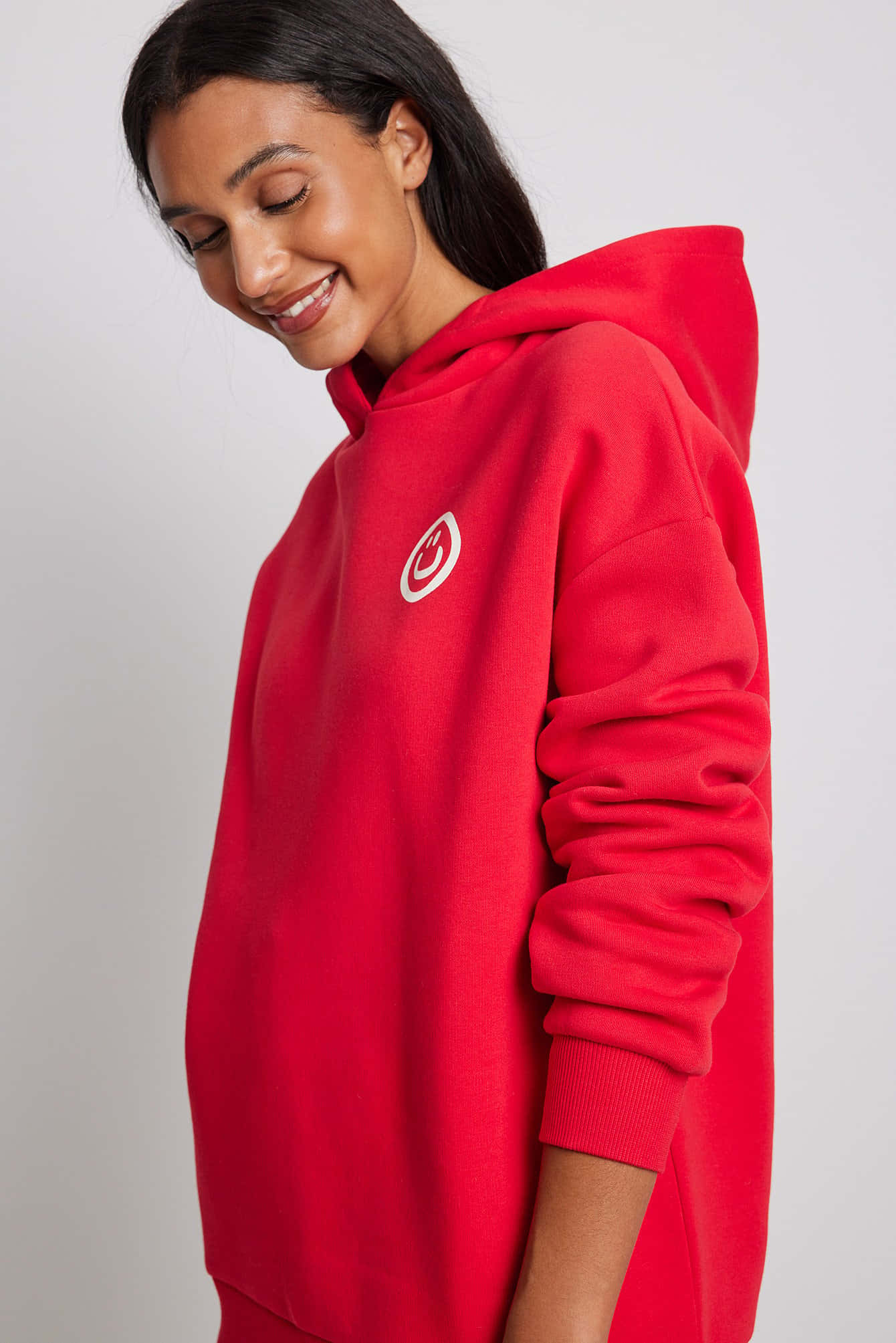 Red Hoodie 桌布 壁紙 — 一位穿著鮮紅色連帽衫的女性在純白色背景前溫柔地微笑。