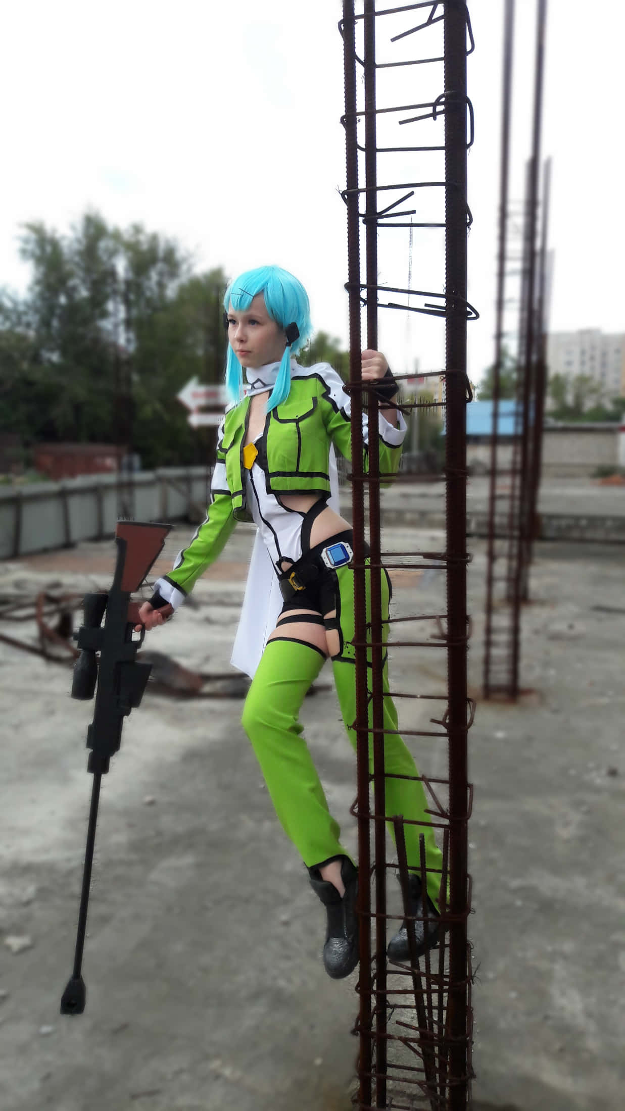 Sword Art Online Cosplay 桌布 壁紙 — 一位穿著鮮豔綠色和白色服裝的角色扮演者在城市建築工地爬上生鏽的金屬梯子，手持道具步槍。