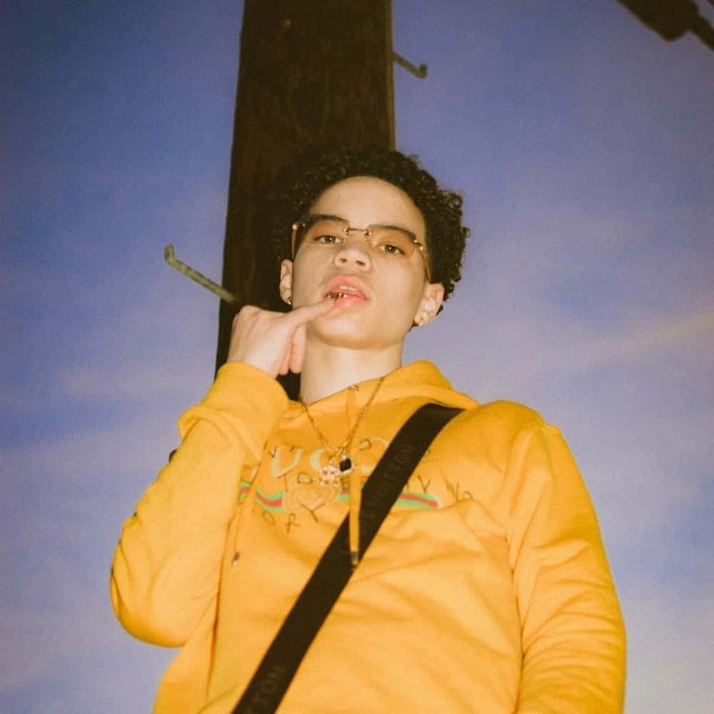 Lil Mosey 桌布 壁紙 — 一位穿著鮮黃色連帽衫的年輕人，在暮色天空下，身後有一根木製電線桿，若有所思地擺著姿勢。