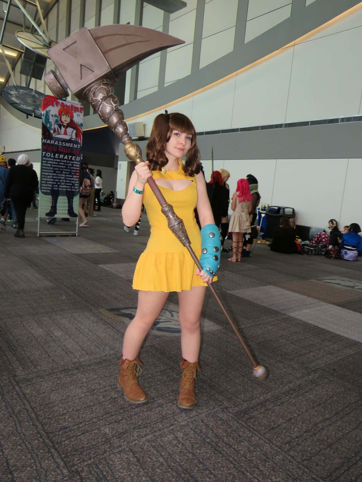 Seven Deadly Sins Diane 桌布 壁紙 — 一位穿著黃色連衣裙的角色扮演者在會議廳中手持一把大型裝飾斧頭，背景有其他與會者。