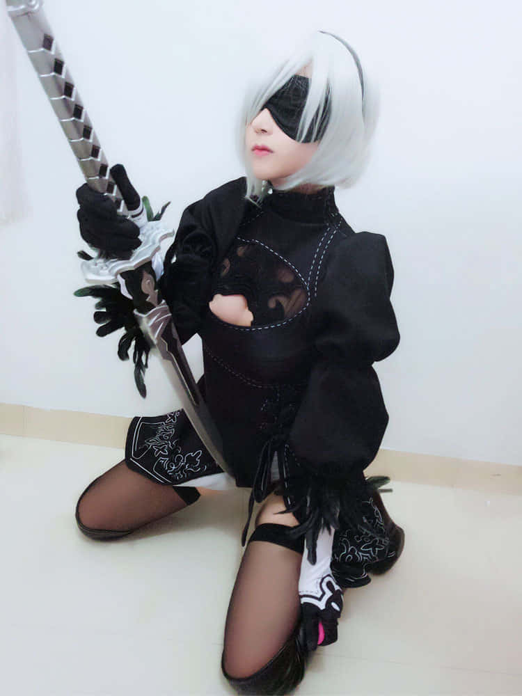 2B 桌布 壁紙 — 一位穿著黑白 NieR:Automata 2B 服裝的角色扮演者跪著，手持劍，靠著純白牆壁。