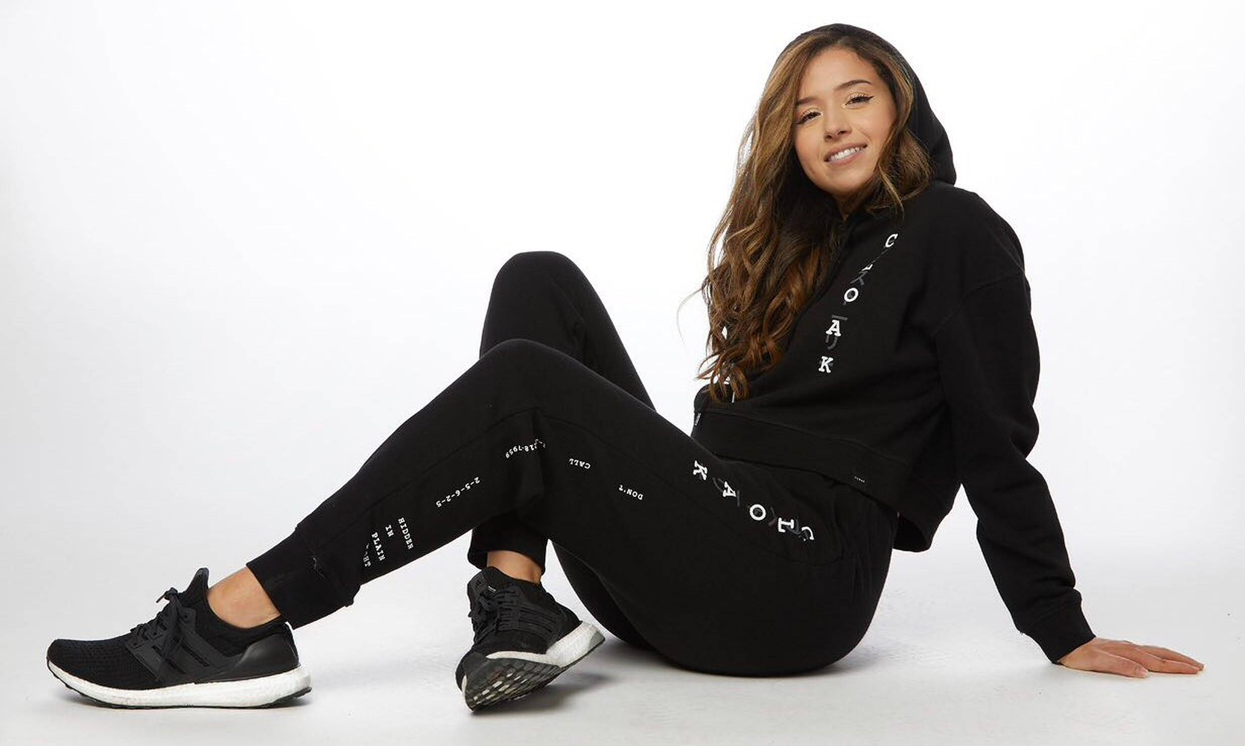 pokimane 桌布 壁紙 — 一位穿著黑色Coak品牌休閒服的年輕女性，在白色工作室地板上隨意坐著微笑。