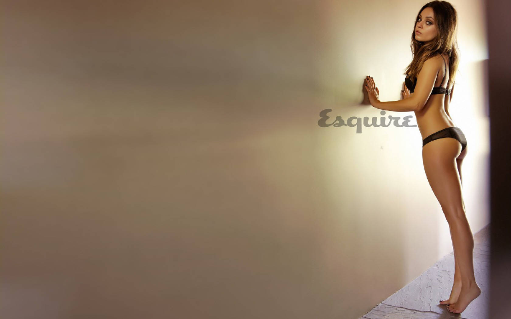 Mila 桌布 壁紙 — 一位穿著黑色內衣的女性在簡約工作室環境中靠著柔和照明的牆壁。