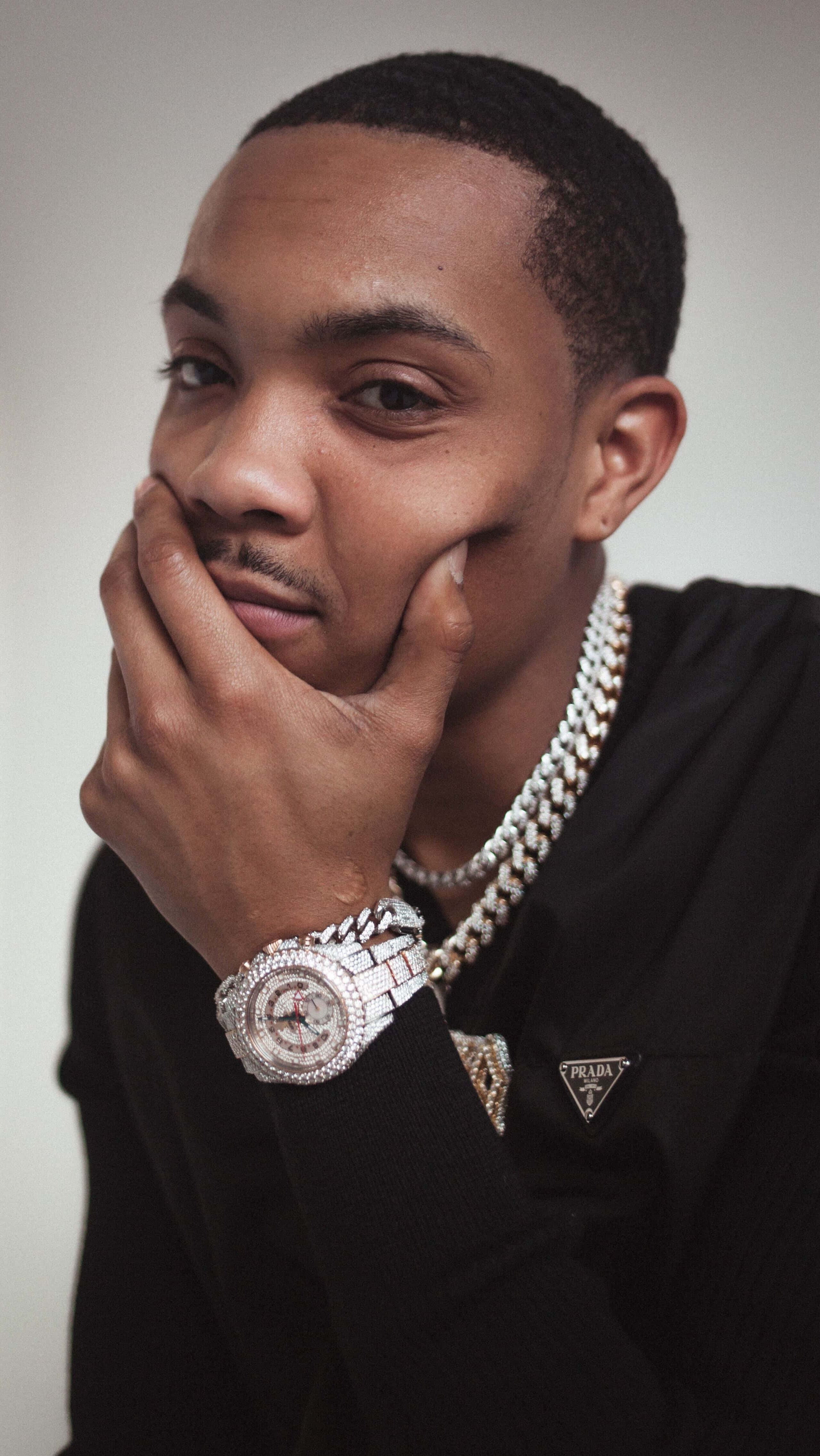 Herbo iPhone 桌布 壁紙 — 一位穿著黑色毛衣的時尚男士，雙手托腮，戴著鑲鑽手錶和粗鏈條。