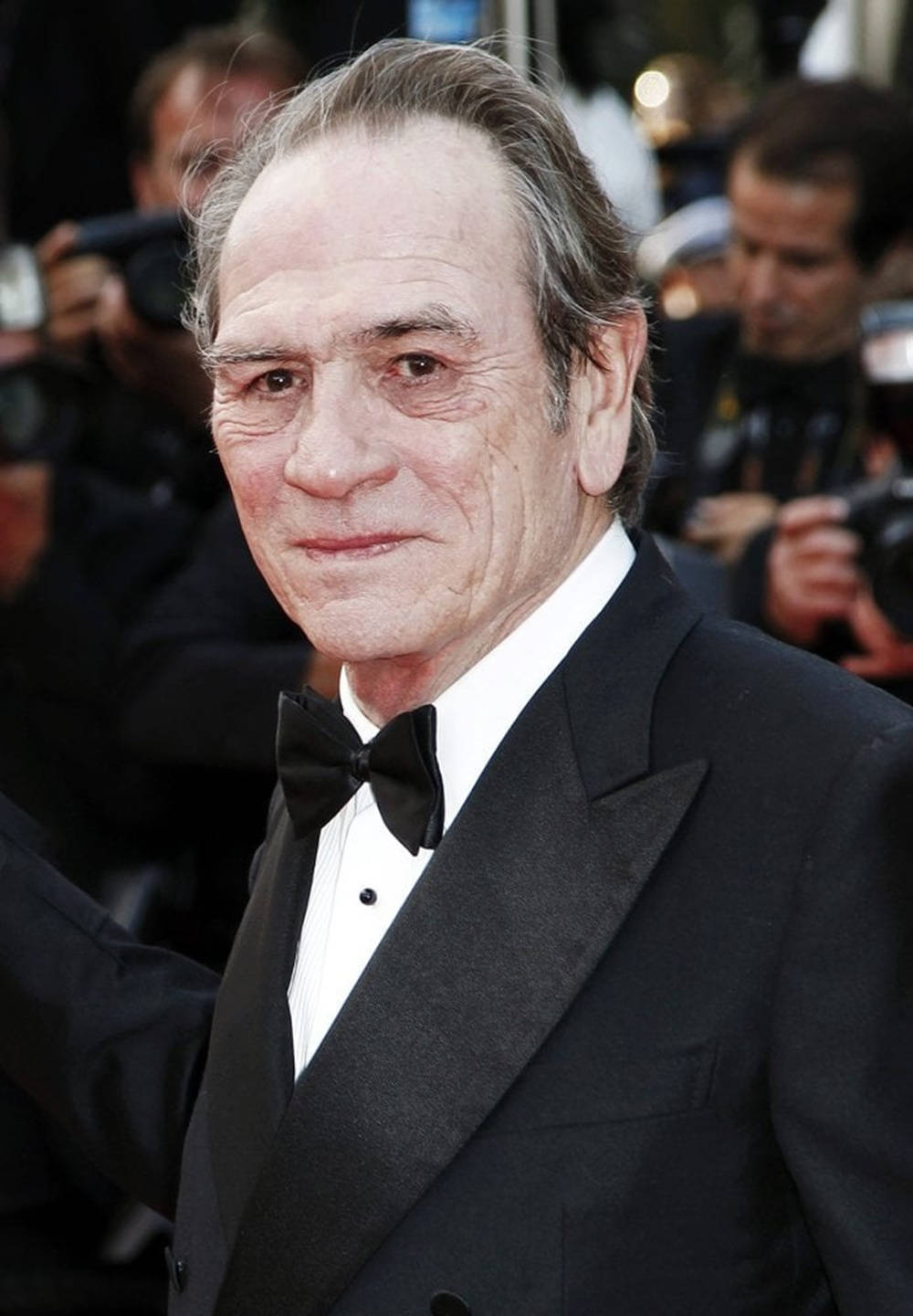 Celebrity 桌布 壁紙 — 一位穿著黑色燕尾服和領結的尊貴長者，在紅地毯上對著鏡頭微笑的特寫肖像，背景有攝影師。